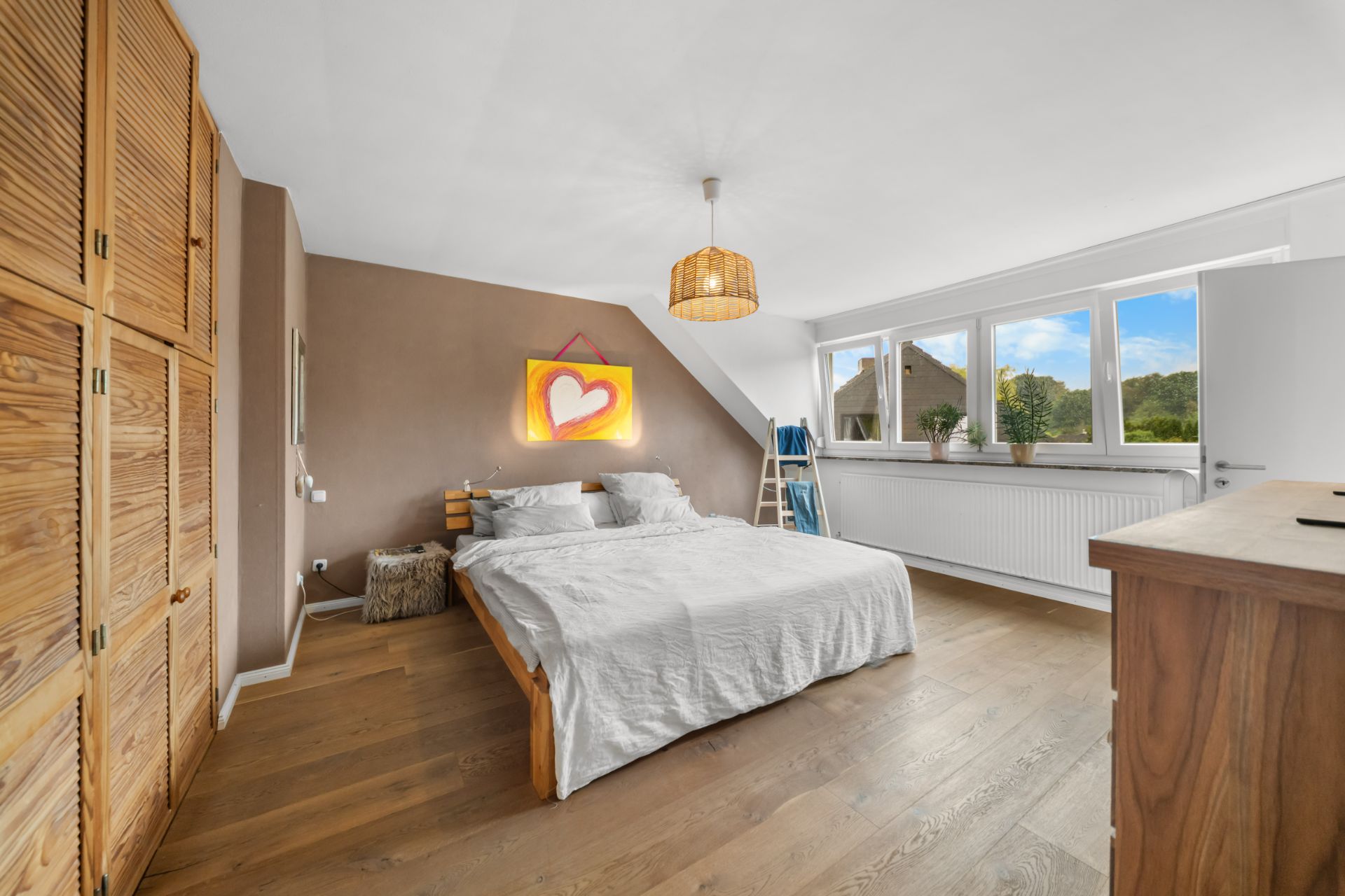 Helles Schlafzimmer mit Holzboden, Doppelbett, Schrank und großen Fenstern.