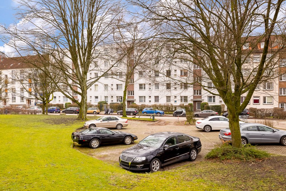 Parkplatz mit mehreren Autos und Bäumen vor Wohngebäuden an einem bewölkten Tag.