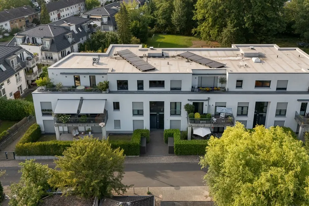 Modernes Wohngebäude mit Flachdach, Balkonen und begrüntem Vorgarten, von oben aufgenommen.