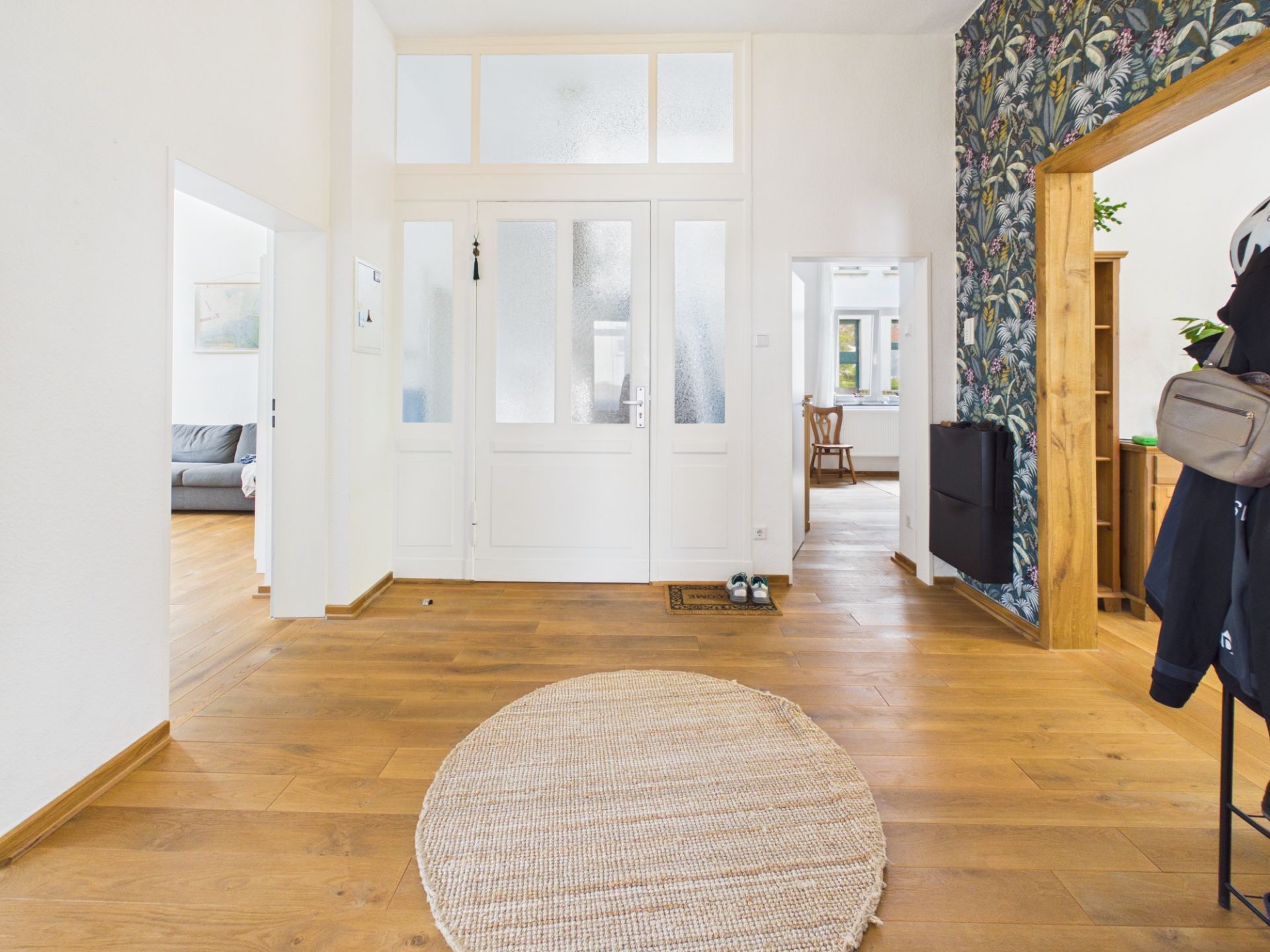 Heller Flur mit Holzboden, runder Teppich und weißen Türen, Wand mit Blumenmuster rechts.