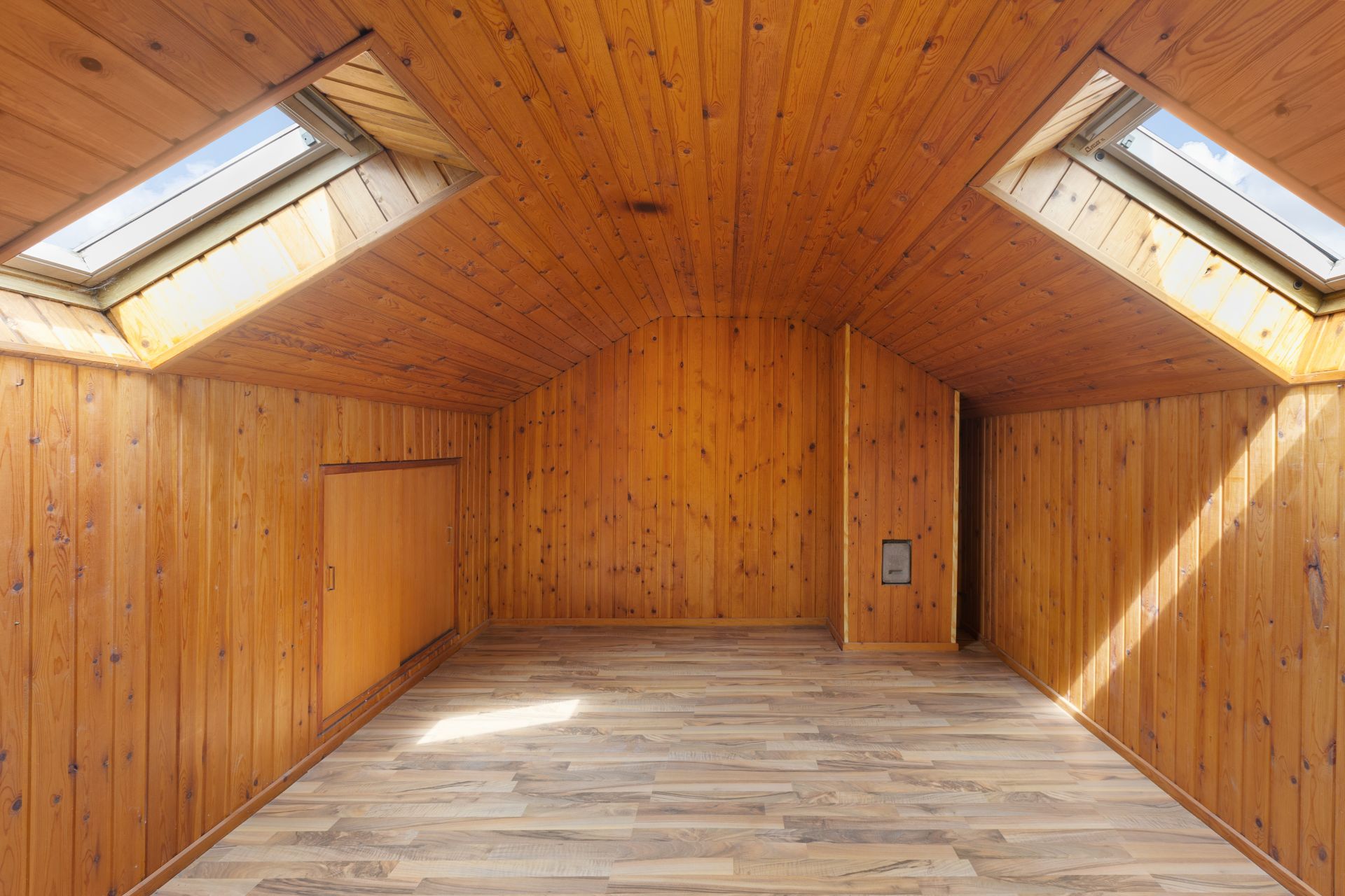 Dachzimmer mit Holzverkleidung, Holzboden und zwei großen Dachfenstern.