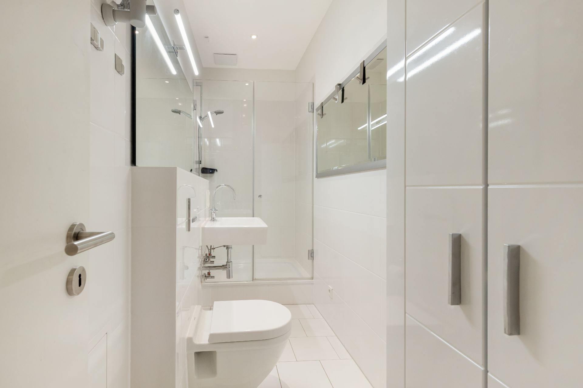 Modernes, weißes Badezimmer mit Dusche, WC, Waschbecken und großem Spiegel.