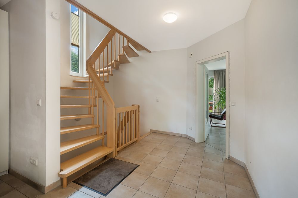 Heller Flur mit gefliesten Boden und Holztreppe, Türöffnung führt in ein weiteres Zimmer.