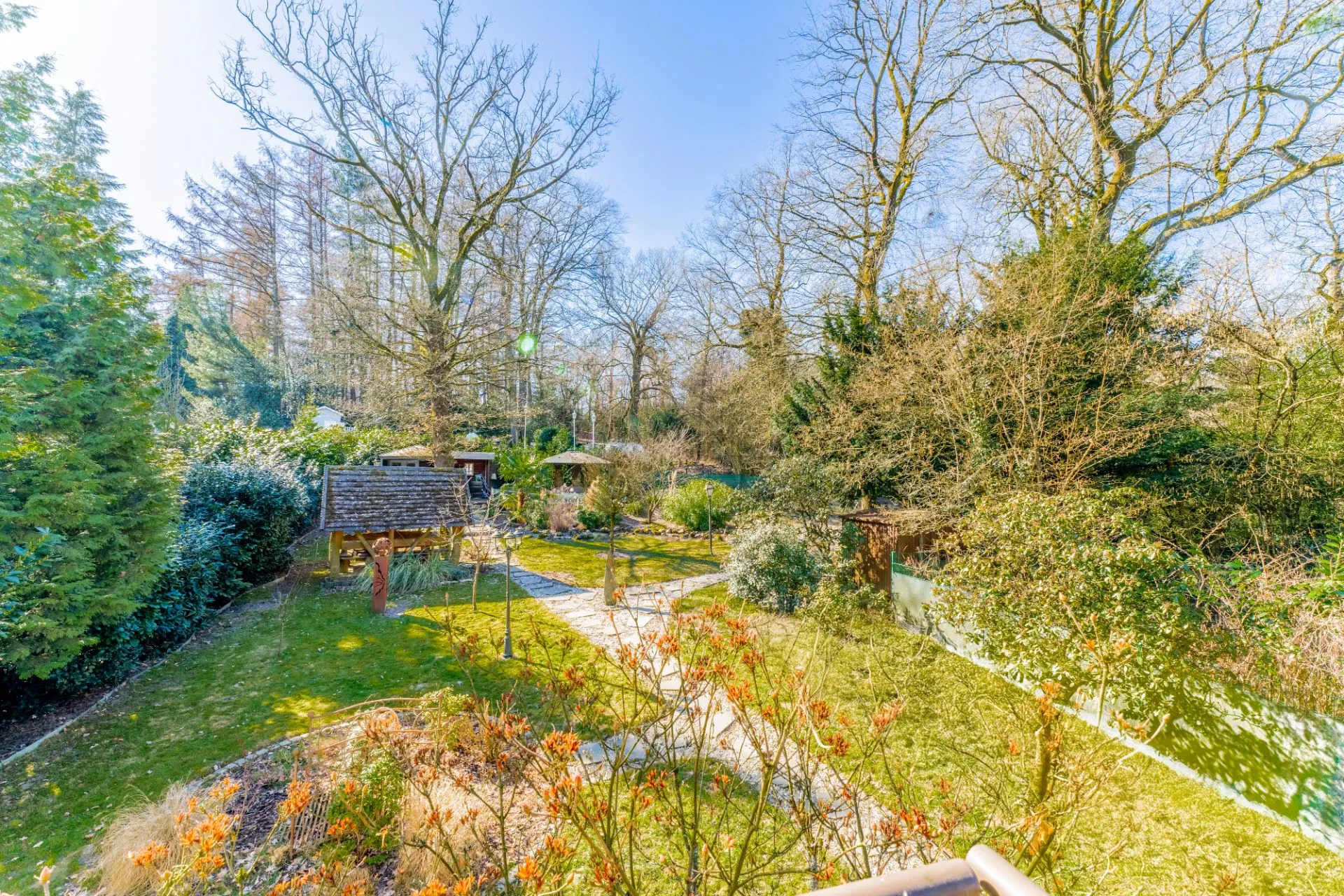 Großer Garten mit Wegen, Bäumen, Sträuchern und Holzhütte an einem sonnigen Tag.