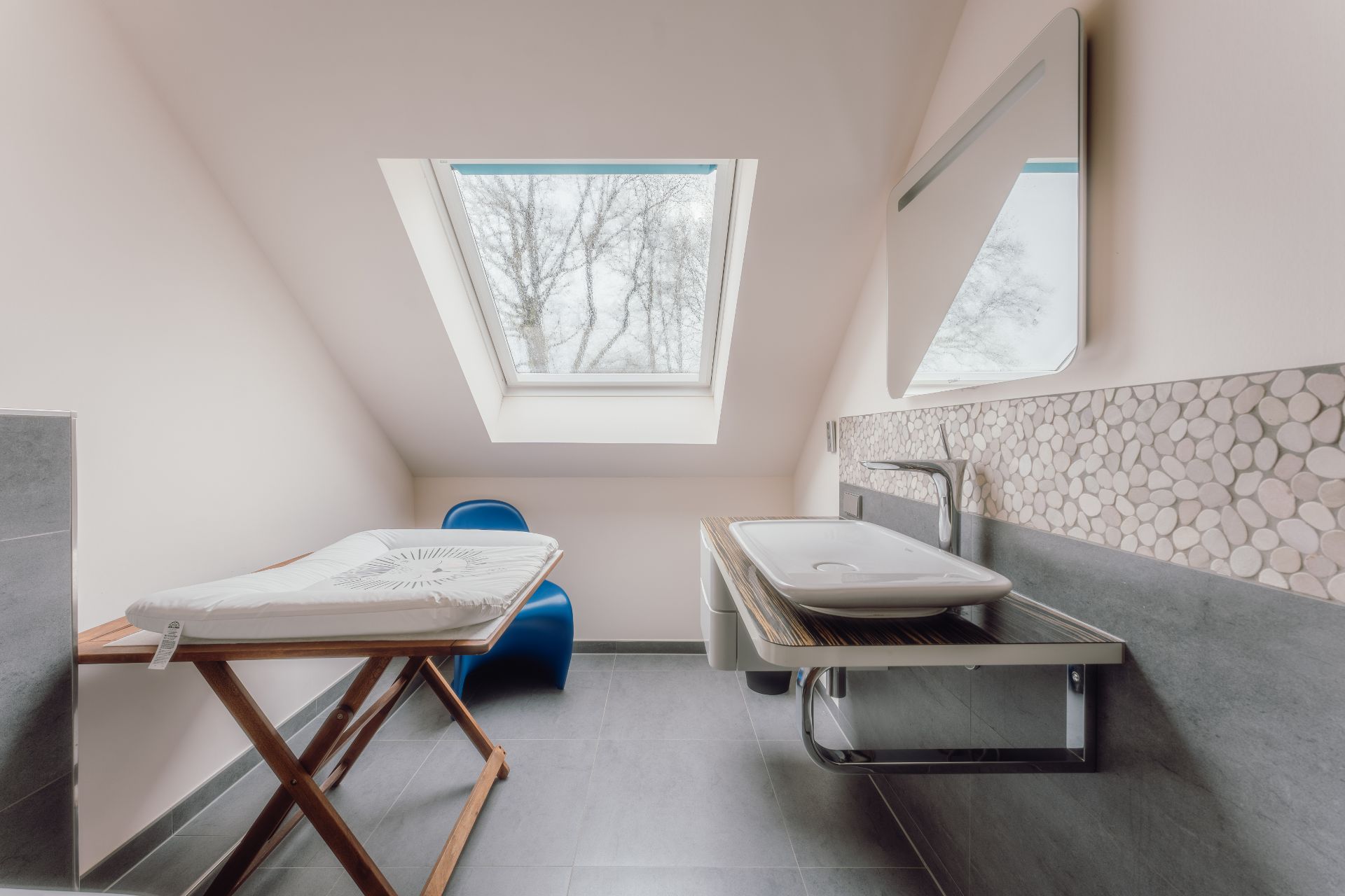 Helles Badezimmer mit Dachfenster, Waschbecken, Spiegel und Wickeltisch.