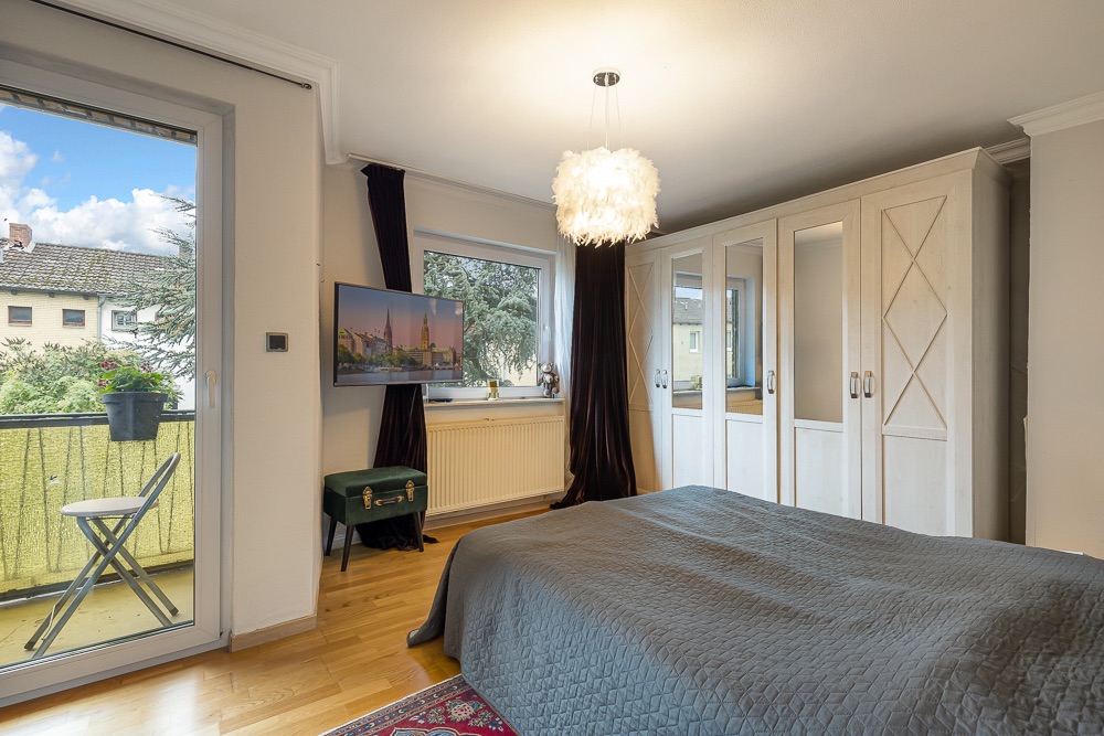 Helles Schlafzimmer mit großem Kleiderschrank, Doppelbett, Balkonzugang und Wandfernseher.