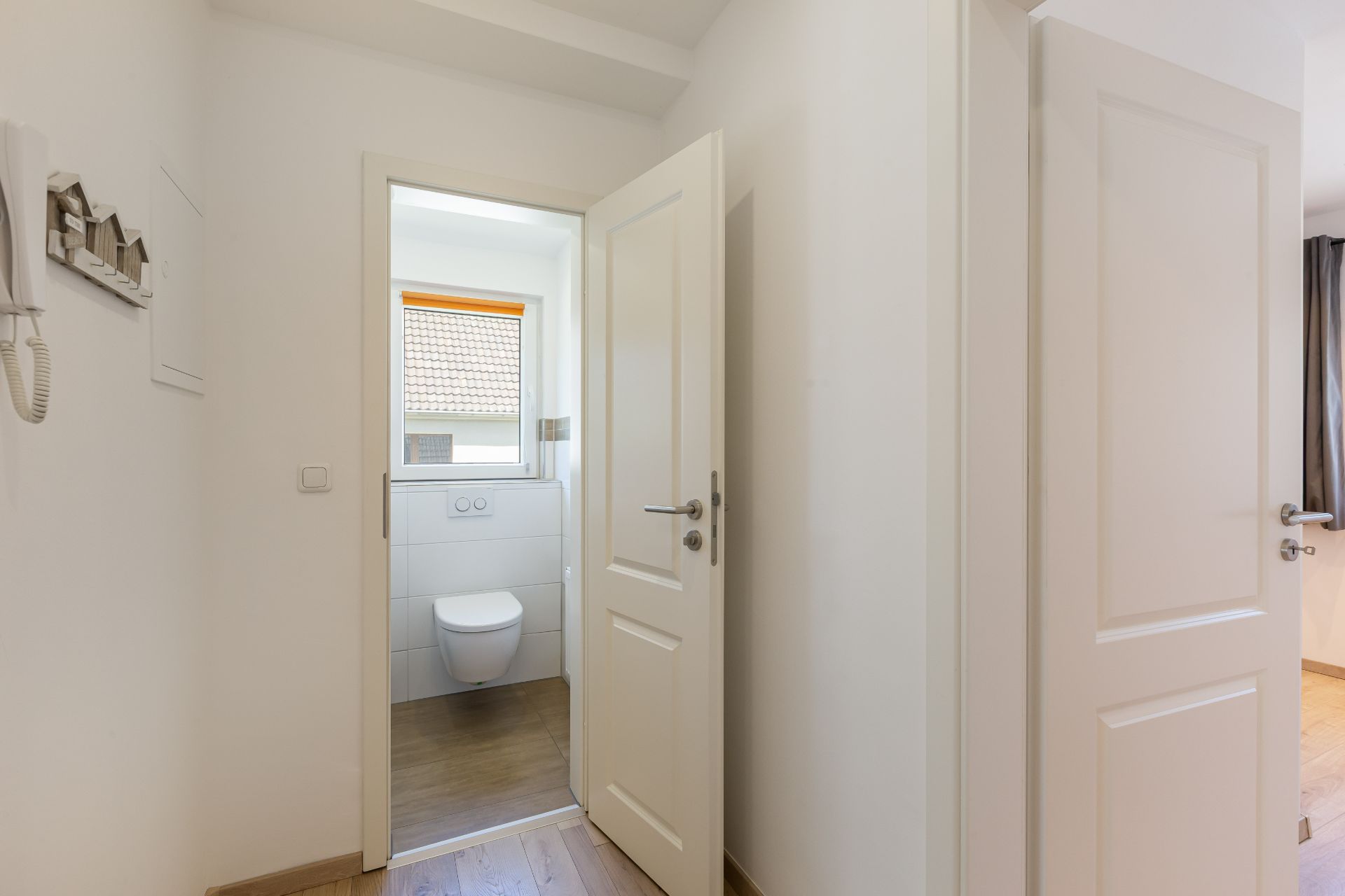 Helle Diele mit Blick durch eine offene Tür auf eine Toilette mit Fenster.