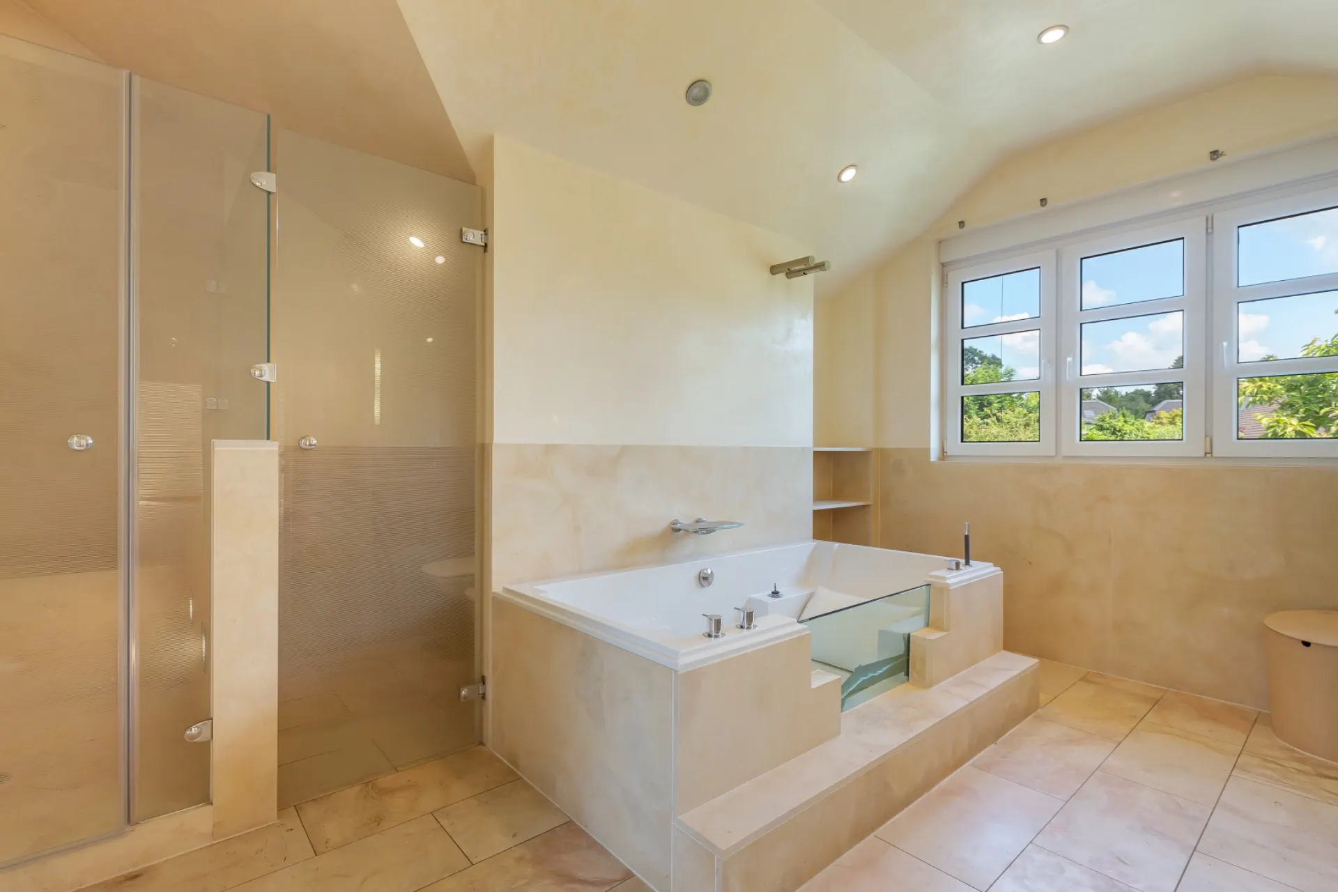 Modernes Badezimmer mit großer Badewanne, Glasdusche und Fenster mit Blick ins Grüne.