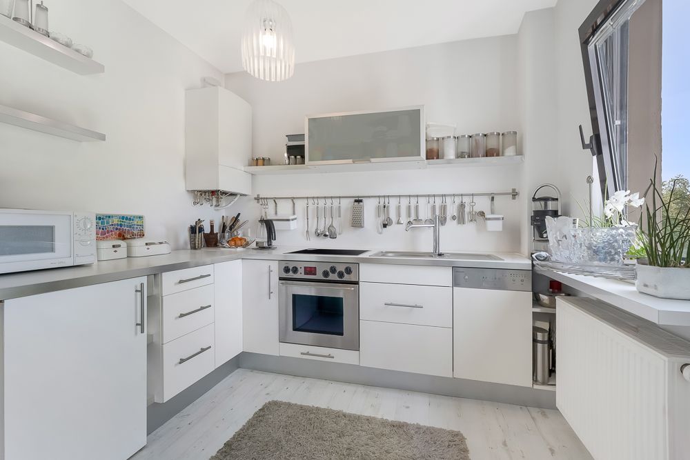Helle, moderne Küche mit weißen Schränken, Backofen, Spüle und offenem Fenster.