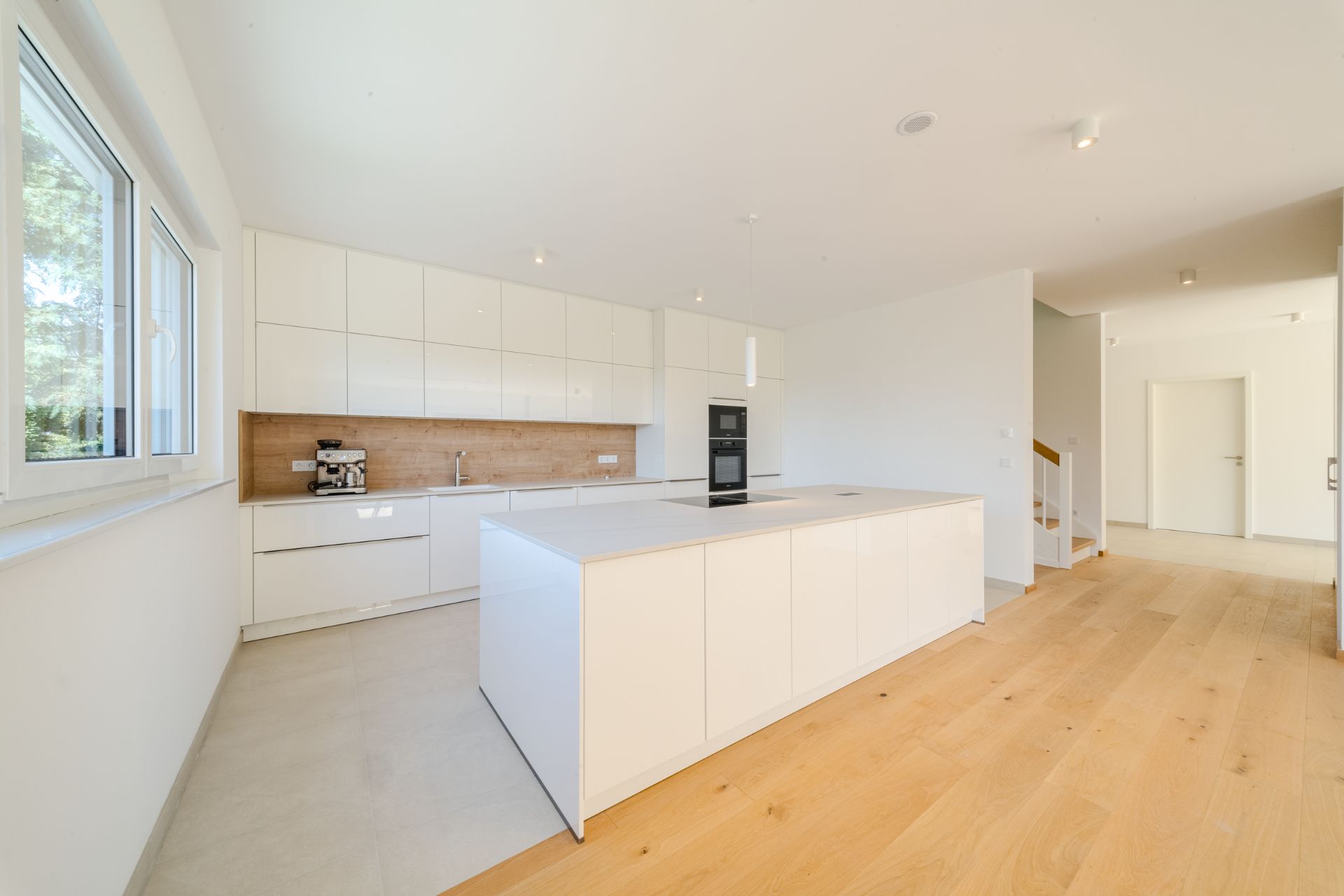 Helle, moderne Küche mit weißer Kücheninsel, Holzfußboden und großen Fenstern.