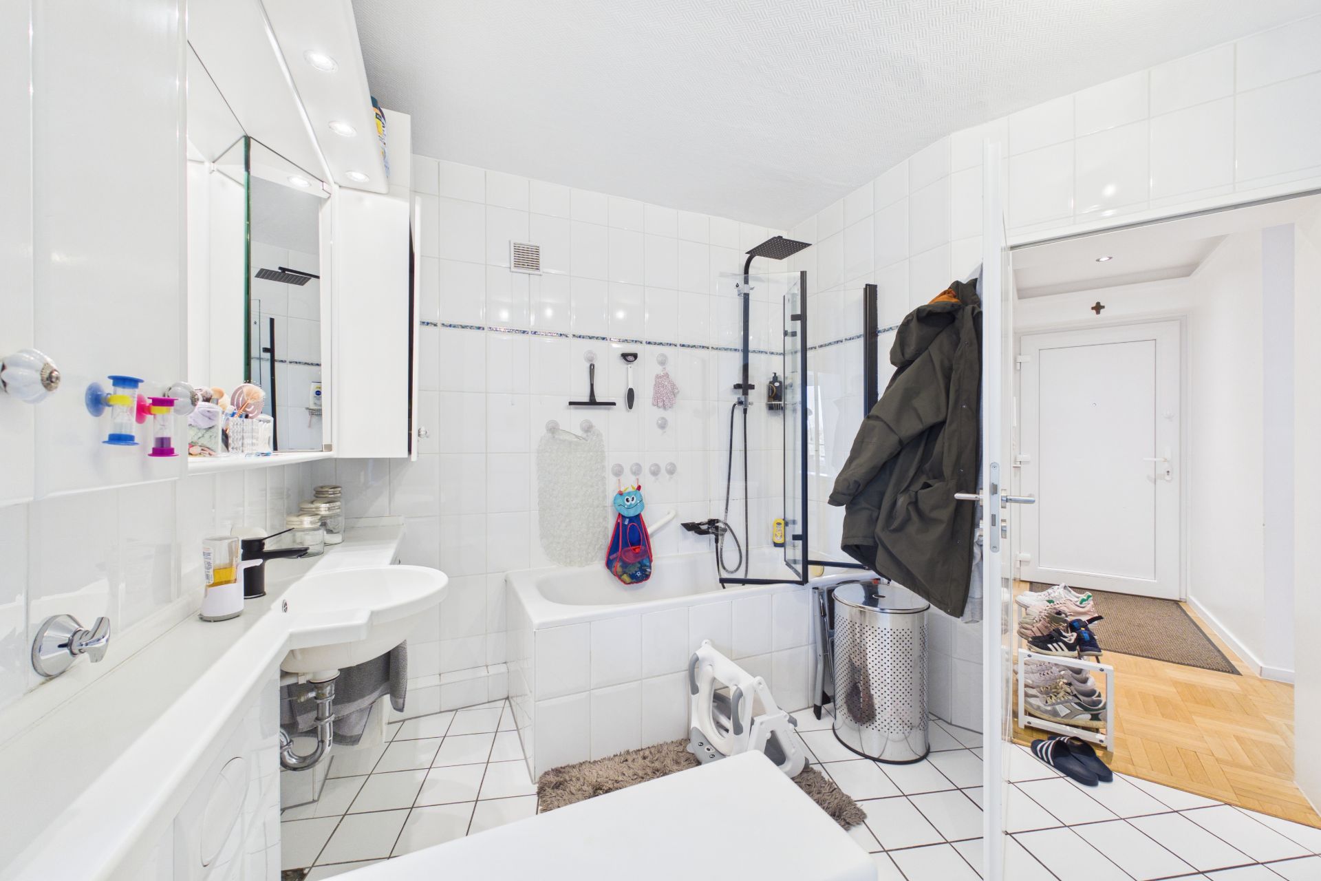 Helles Badezimmer mit Badewanne, Waschbecken, Spiegel und sichtbarem Eingangsbereich.