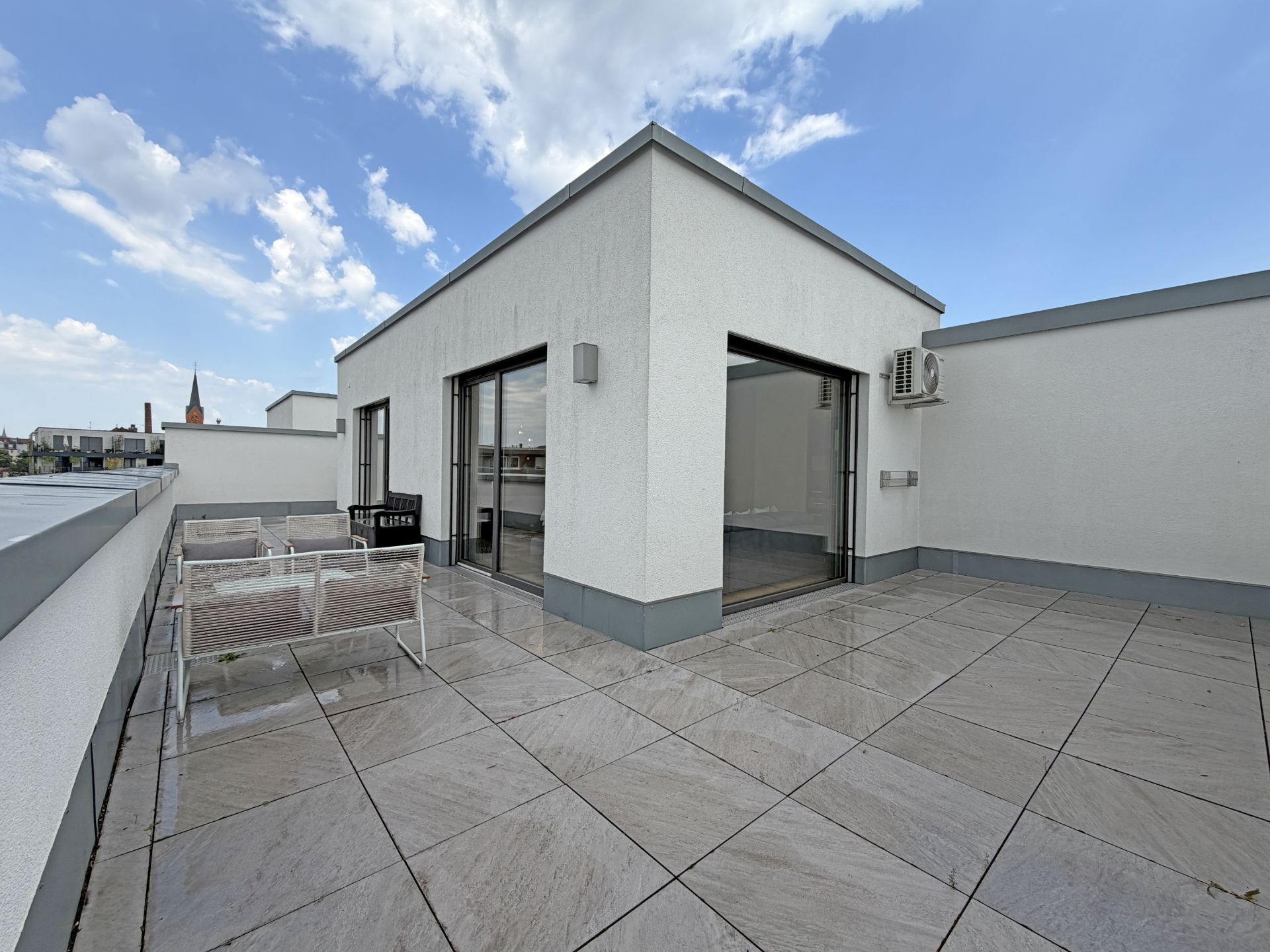 Große Dachterrasse mit Fliesen, weißen Wänden und Sitzmöbeln bei Tageslicht.