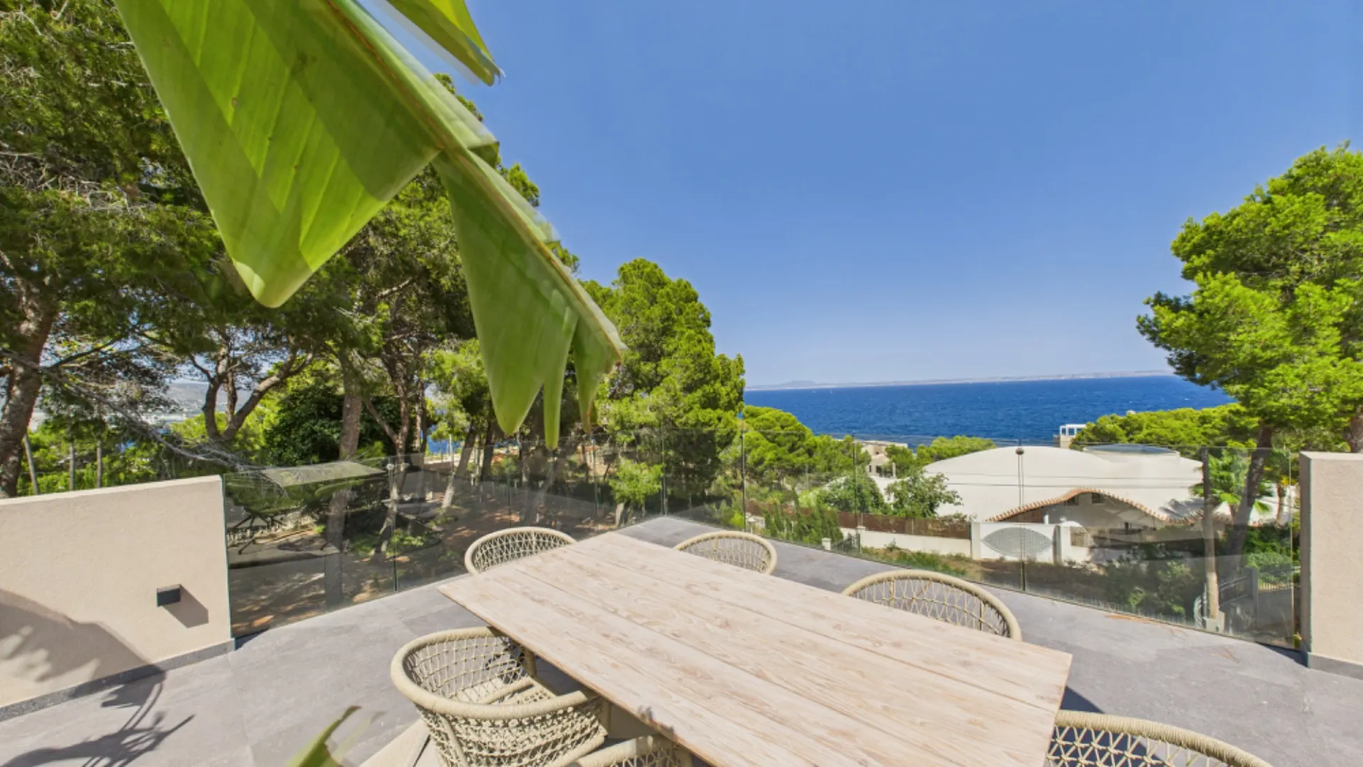 Terrasse mit Holztisch und Stühlen, Blick auf das Meer und umgebende Bäume.