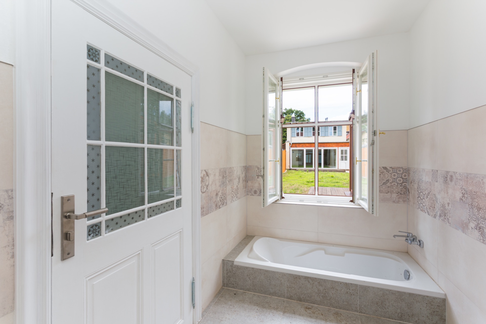 Helles Badezimmer mit Badewanne und offenem Fenster mit Blick auf einen Garten.