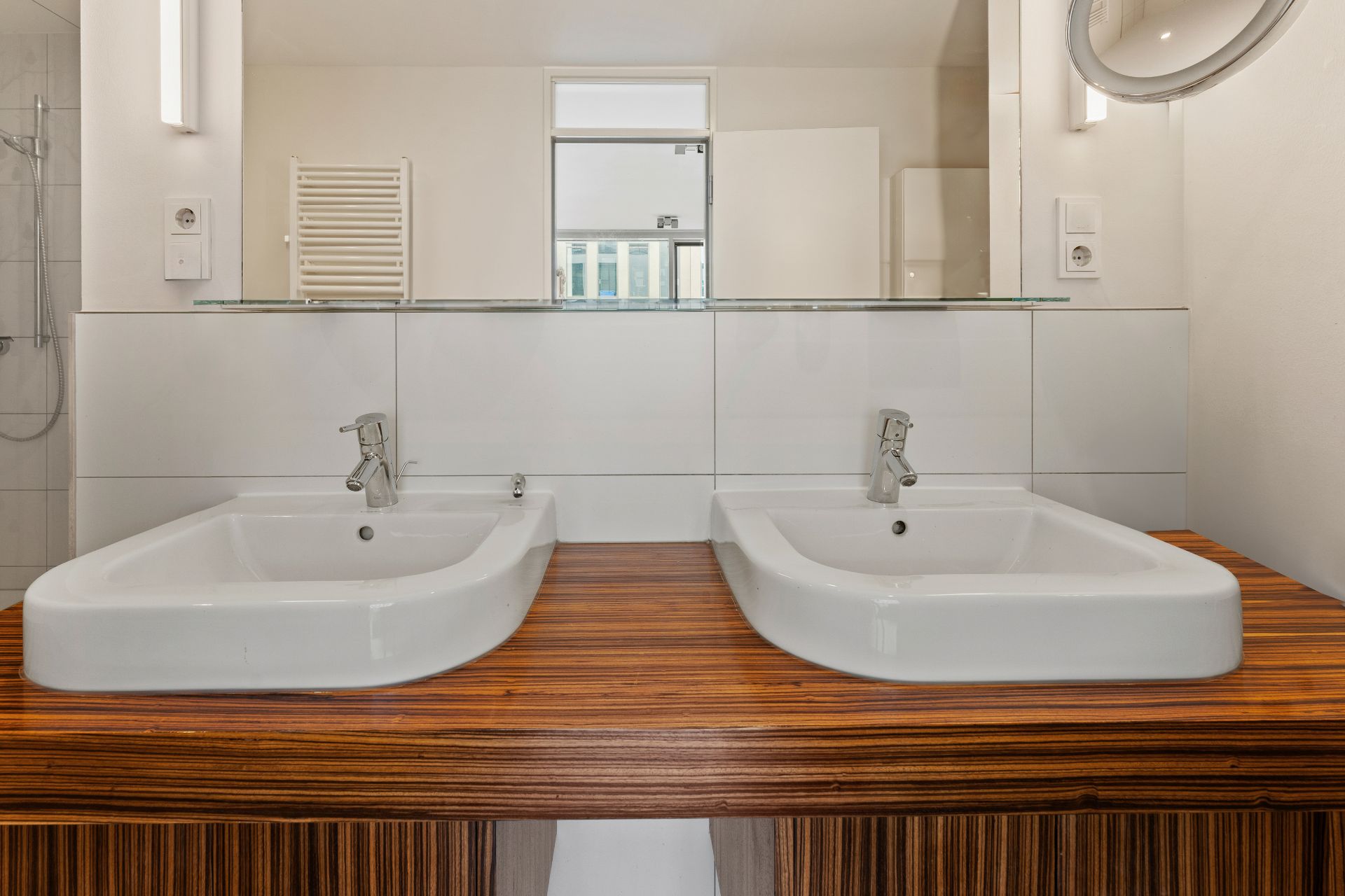 Zwei Waschbecken auf Holzplatte in modernem Badezimmer mit Spiegel und Armaturen.