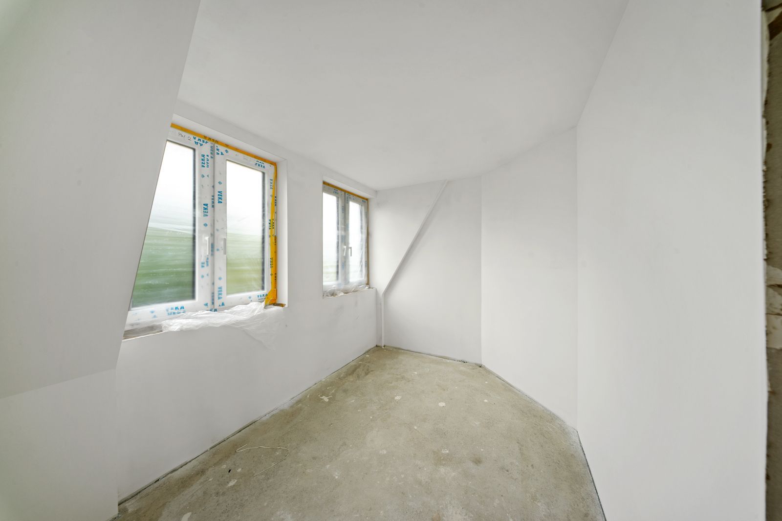 Leerer Raum mit weißen Wänden, zwei Fenstern und Betonboden.