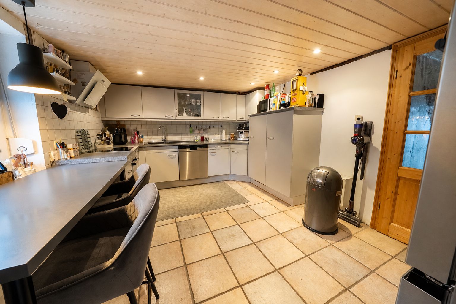 Moderne Wohnküche mit grauen Schränken, Theke, Barhockern und Fliesenboden.