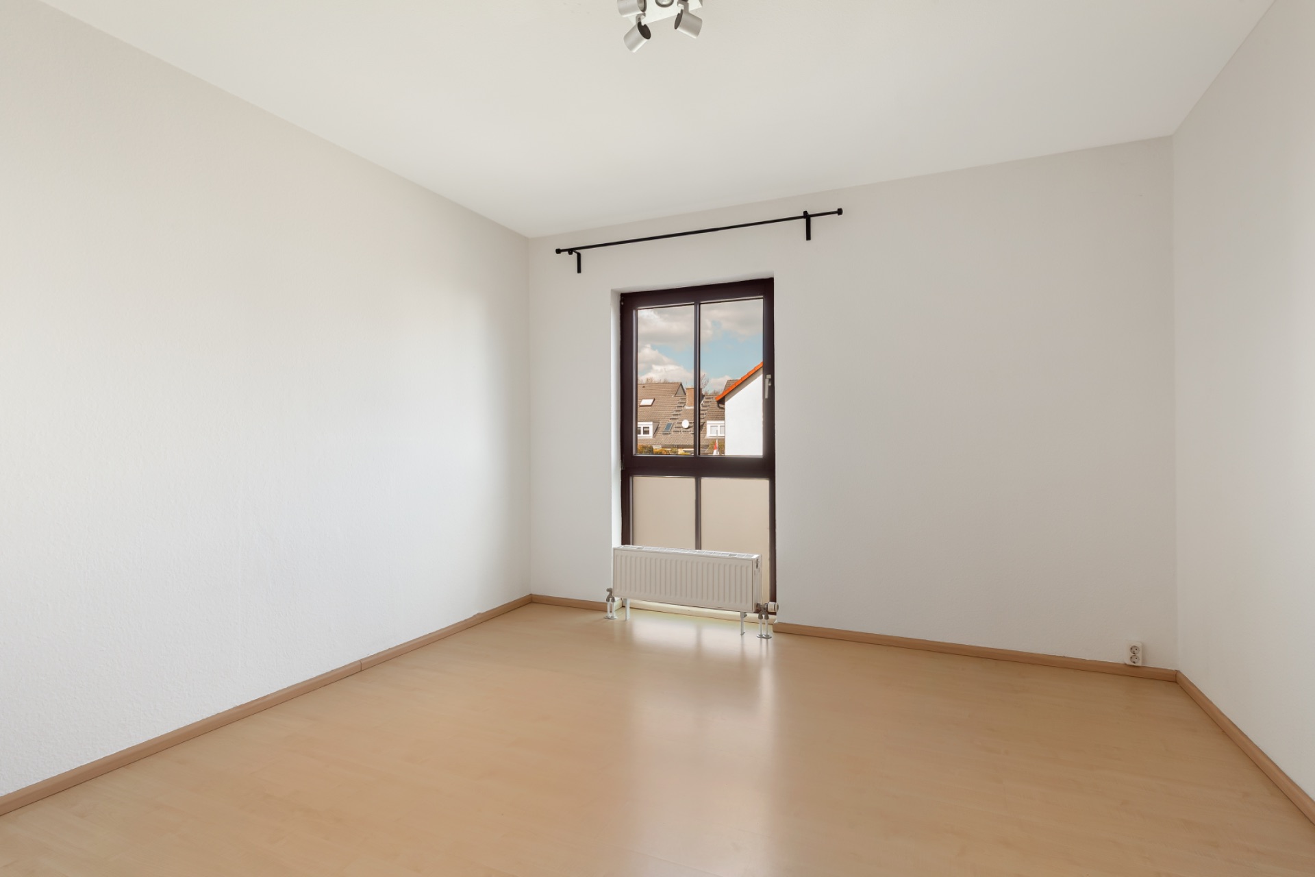 Leerer Raum mit hellem Holzboden, weißem Wänden und Fenster mit Heizung darunter.