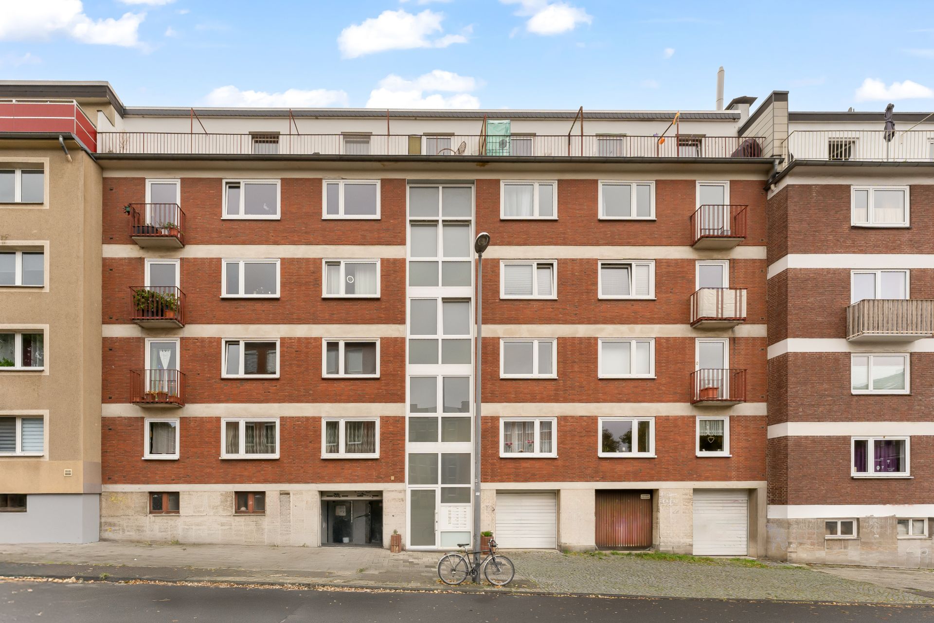 Mehrfamilienhaus mit roter Fassade, mehreren Balkonen und Fahrrad vor dem Eingang.