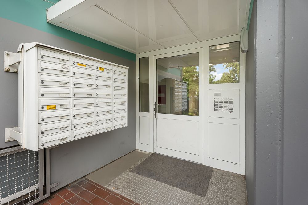 Eingangsbereich mit weißen Briefkästen und Glastür in einem Wohnhaus.
