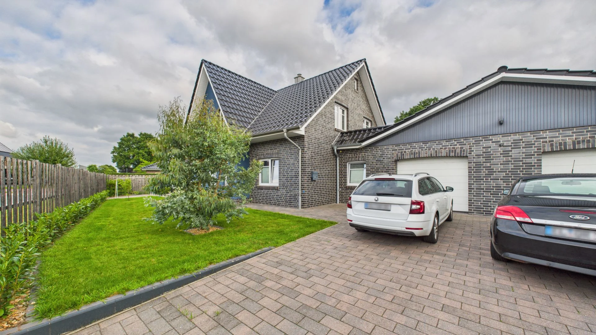 Einfamilienhaus mit Ziegeldach, Doppelgarage, zwei Autos und gepflegtem Vorgarten.