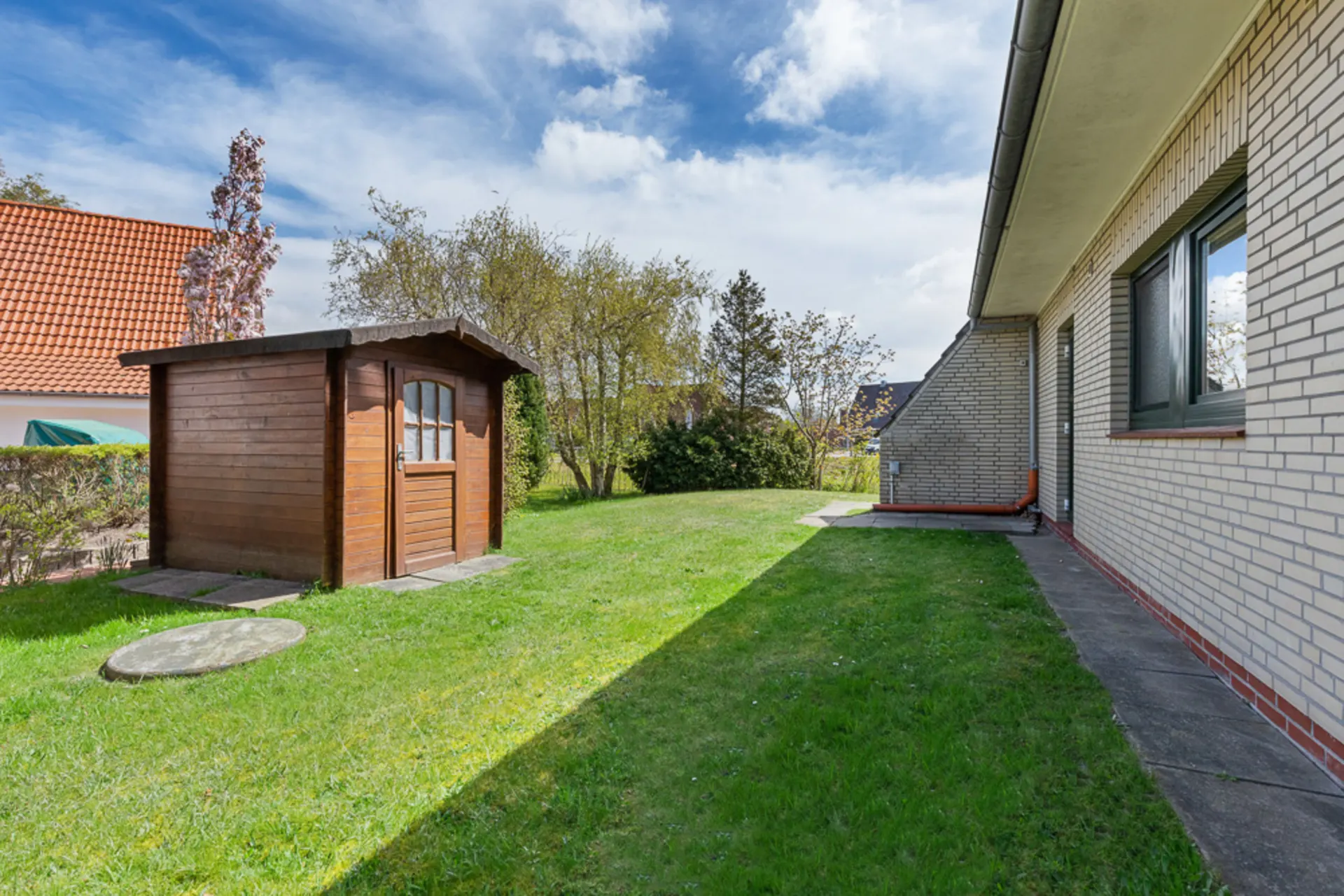 Garten mit Rasen, Holzhaus und gemauertem Wohnhaus an der Seite.