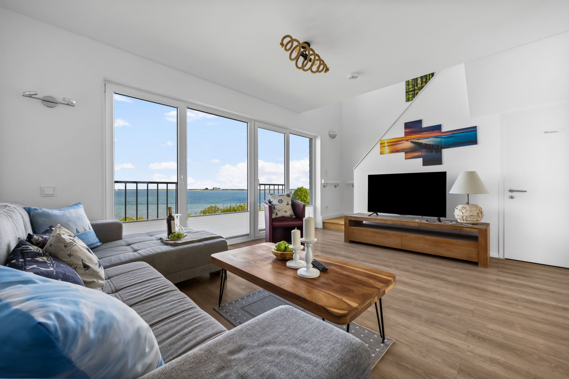 Modernes Wohnzimmer mit großem Sofa, Couchtisch, TV und Meerblick durch große Fenster.