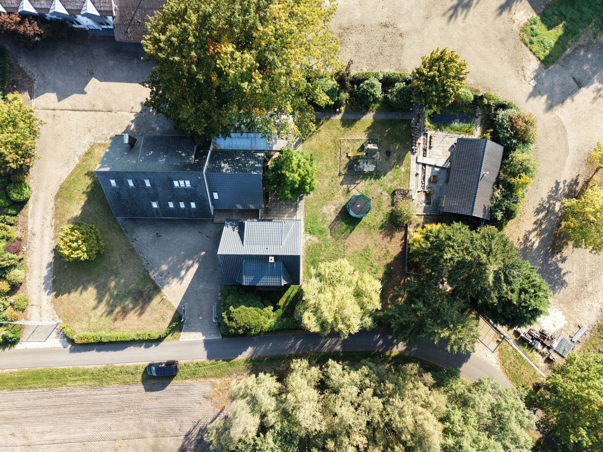 Luftaufnahme eines Wohnhauses mit Garten, Bäumen und Zufahrtsstraße.