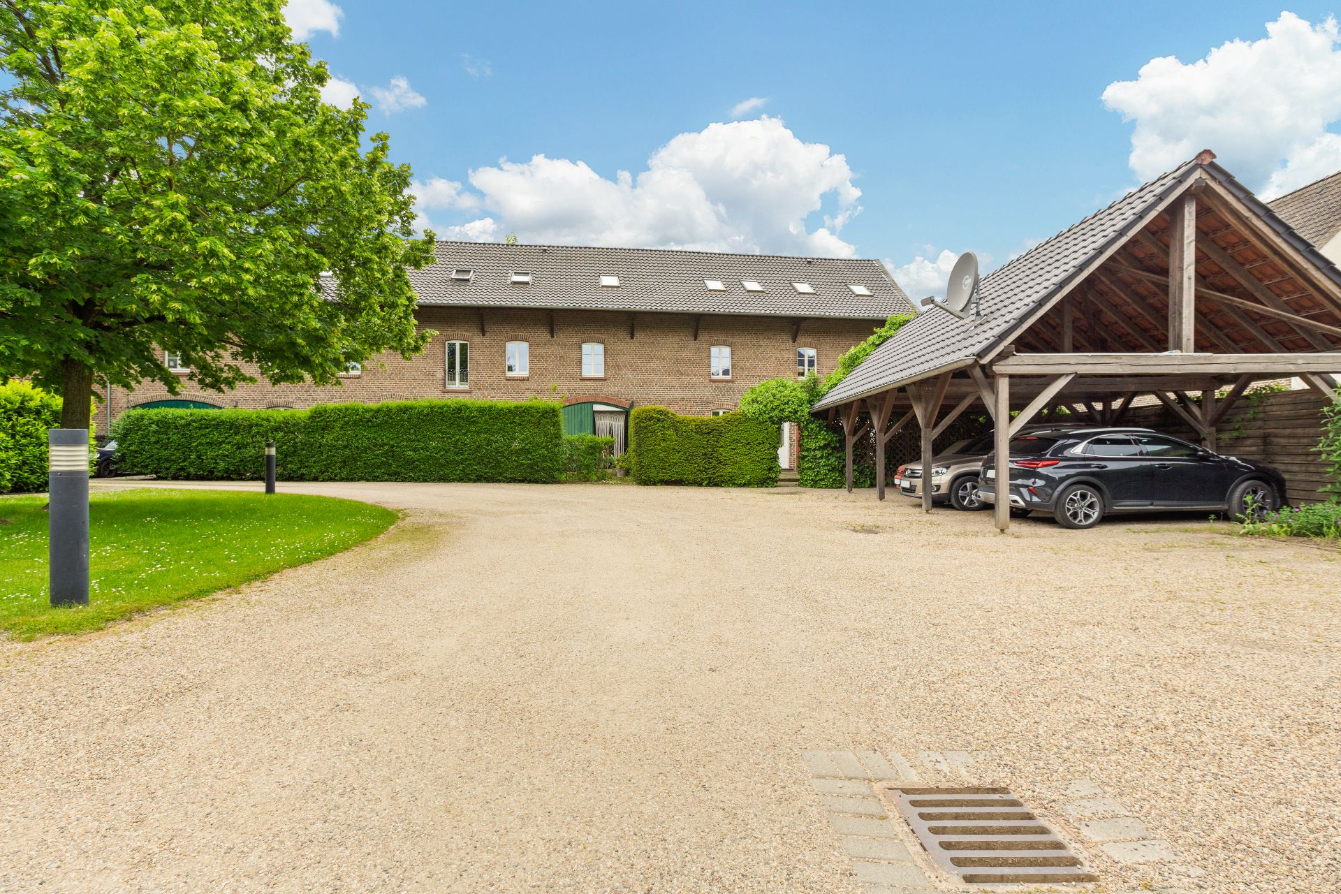 Gepflasterter Hof mit Carport, parkenden Autos, Baum und Backsteingebäude im Hintergrund.