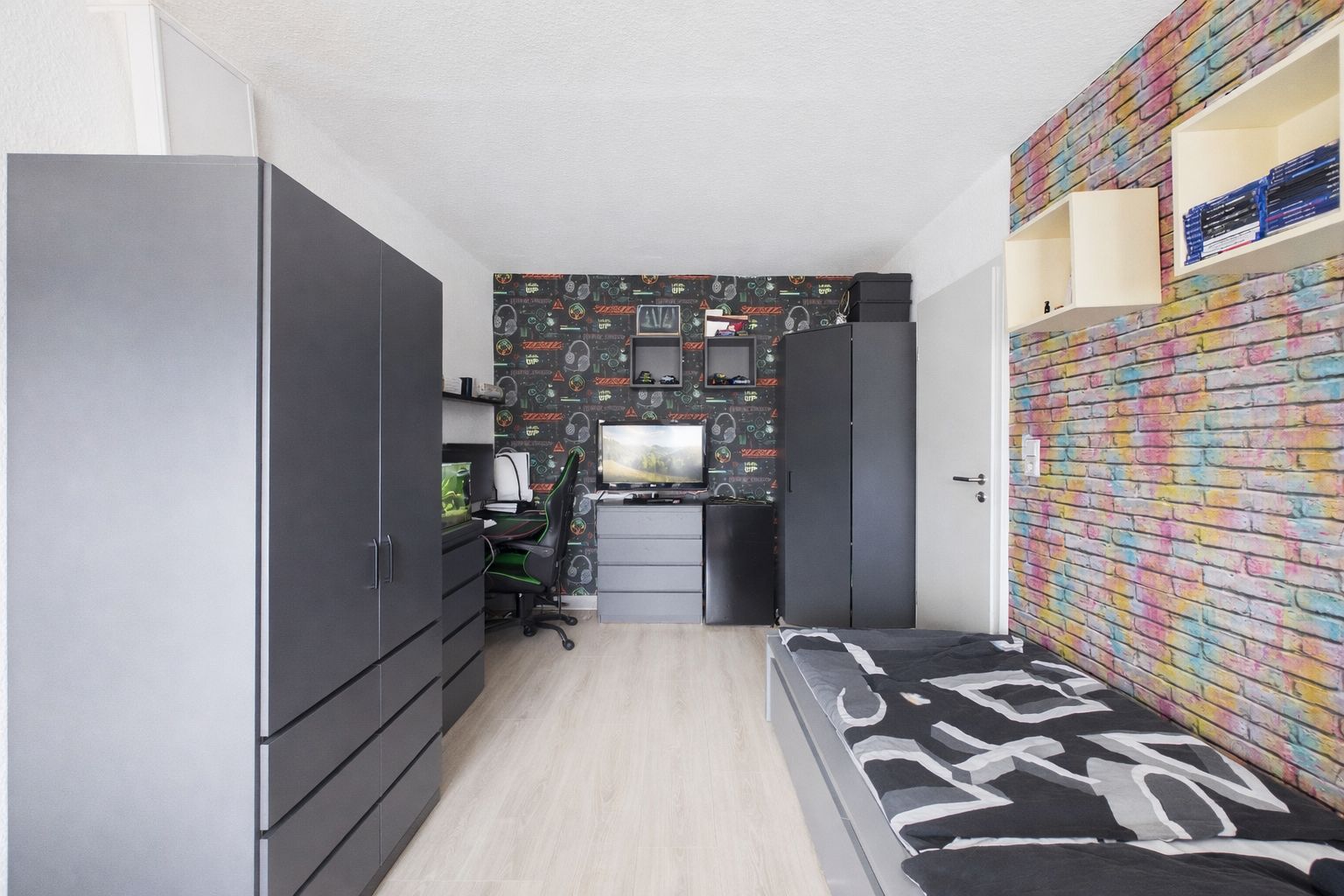 Modernes Zimmer mit Bett, zwei Schränken, Schreibtisch und bunter Backsteinwand.