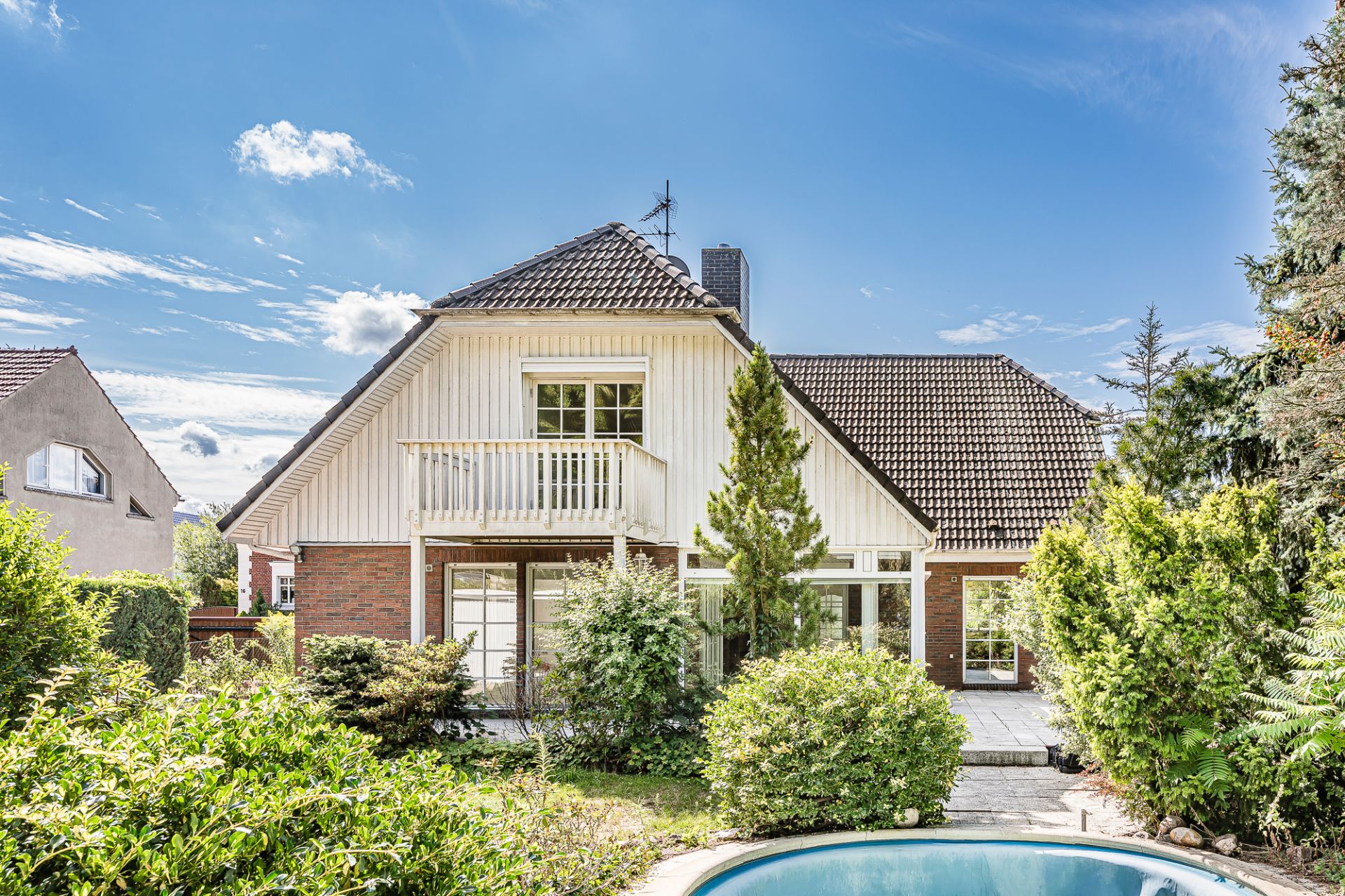 Zweistöckiges Haus mit Balkon, Garten und kleinem runden Pool im Vordergrund.