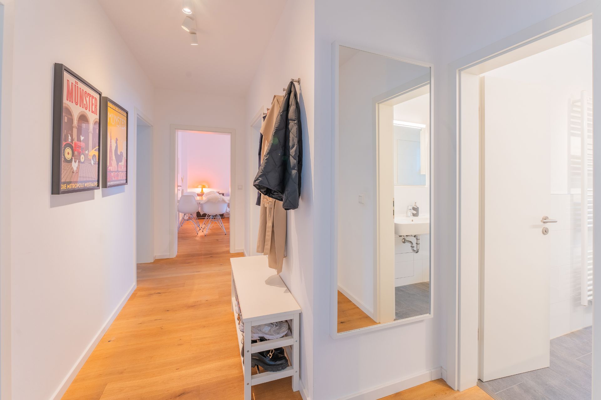 Heller Flur mit Holzboden, Garderobe, Spiegel, Wandbildern und Blick ins Wohnzimmer.