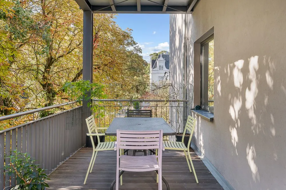 Überdachter Balkon mit Tisch, vier Stühlen und Blick auf Bäume.