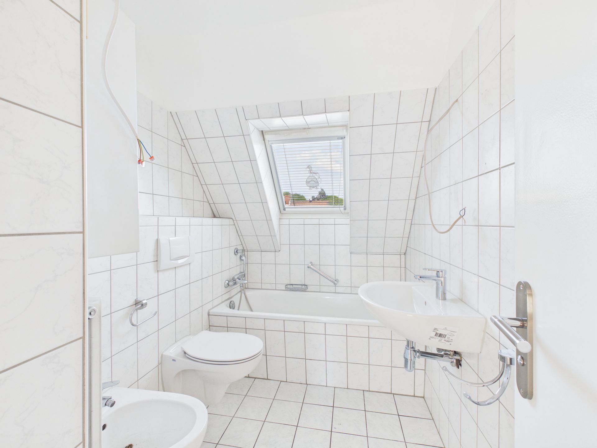 Helles Badezimmer mit Badewanne, Toilette, Bidet, Waschbecken und Fenster unter einer Schräge.