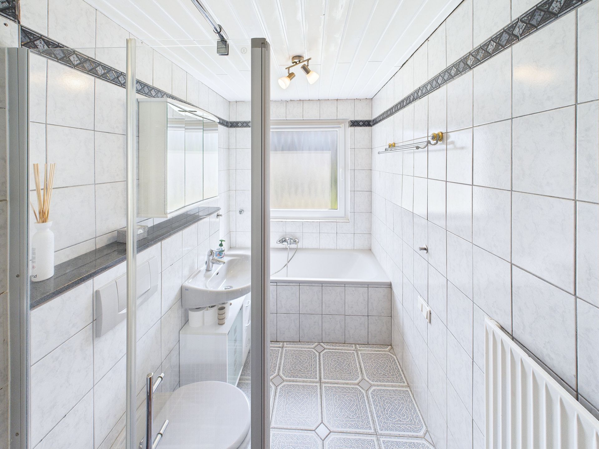 Helles Badezimmer mit Fliesen, Dusche, Badewanne, Waschbecken und Fenster.