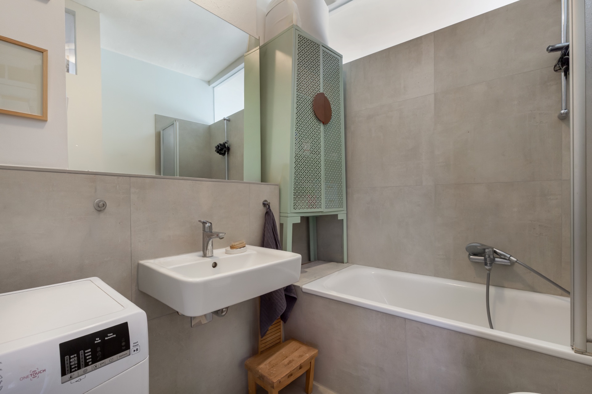 Modernes Badezimmer mit Waschbecken, Badewanne, Waschmaschine und einem kleinen Holzstuhl.
