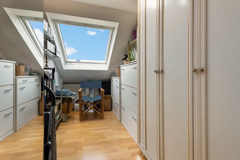 Kleines Zimmer mit Dachfenster, weißen Schränken, Regalen und Holzstuhl auf Parkettboden.
