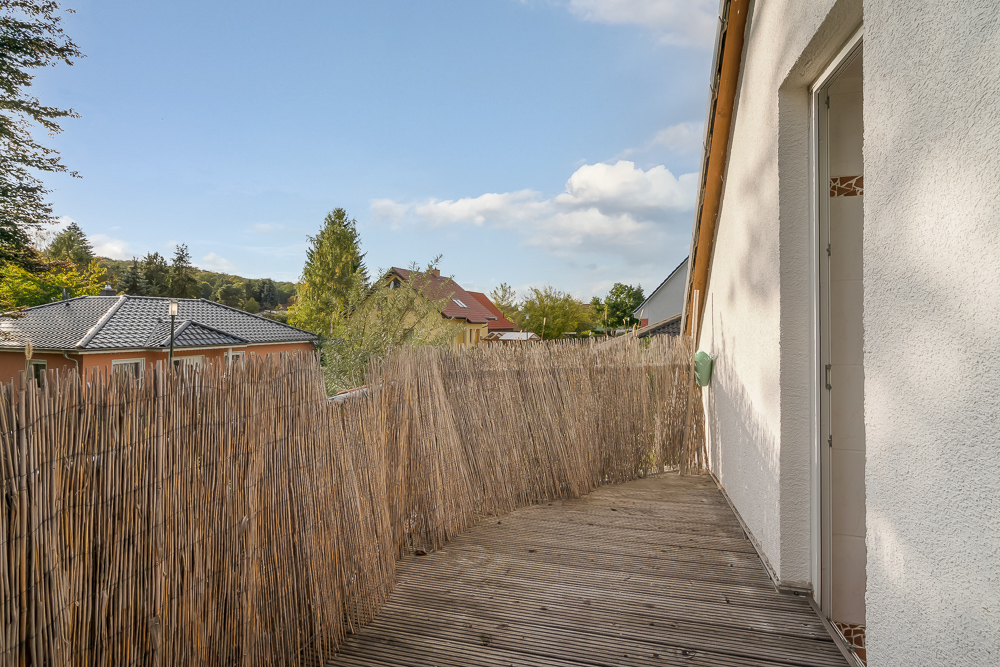 Holzbalkon mit Sichtschutz aus Schilfrohr und Blick auf Nachbarhäuser und Bäume.