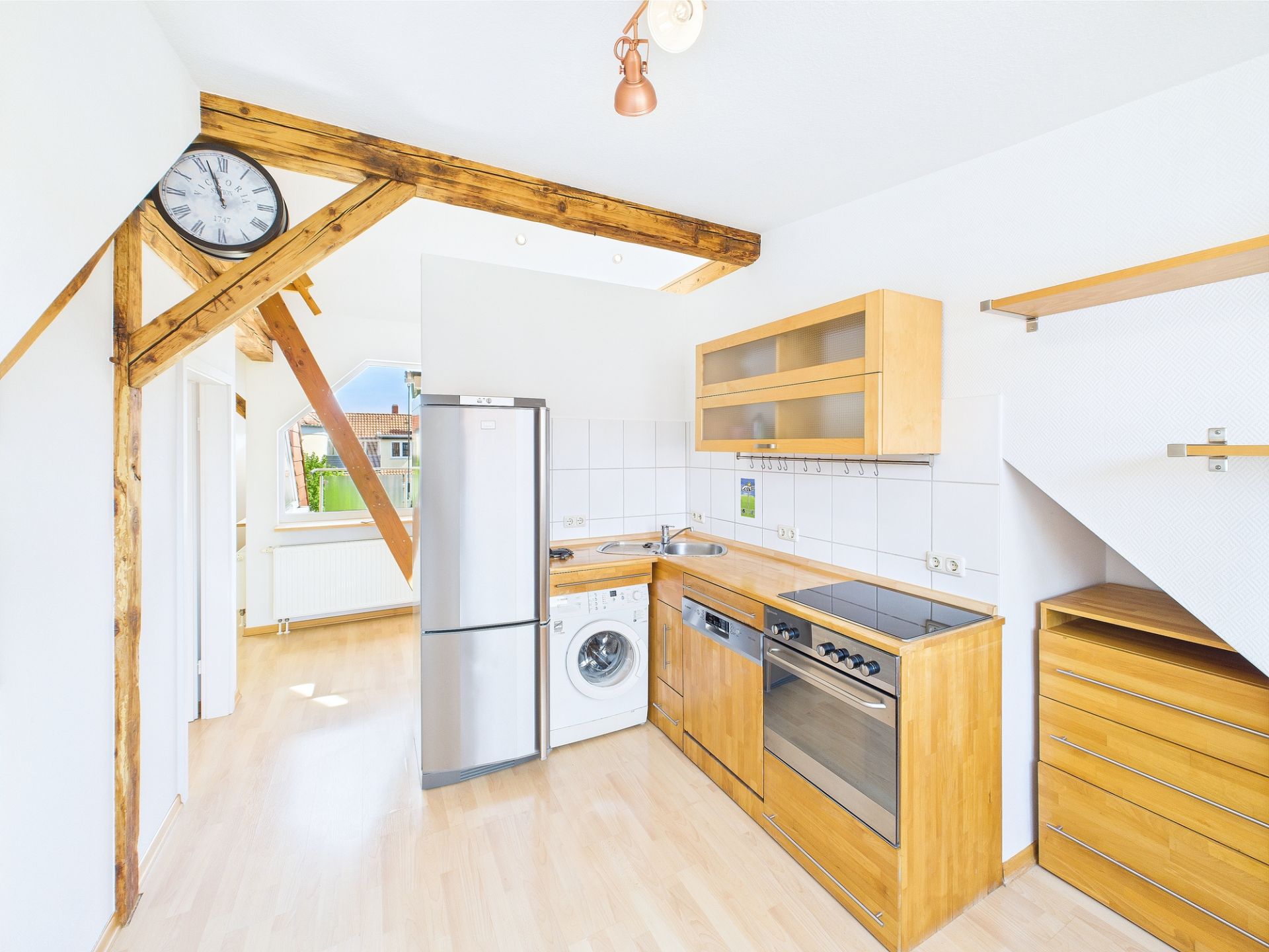 Helle Holzküche mit Kühlschrank, Herd, Waschmaschine und sichtbaren Holzbalken.