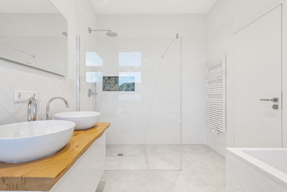 Modernes weißes Badezimmer mit Doppelwaschbecken, ebenerdiger Dusche und Handtuchheizkörper.