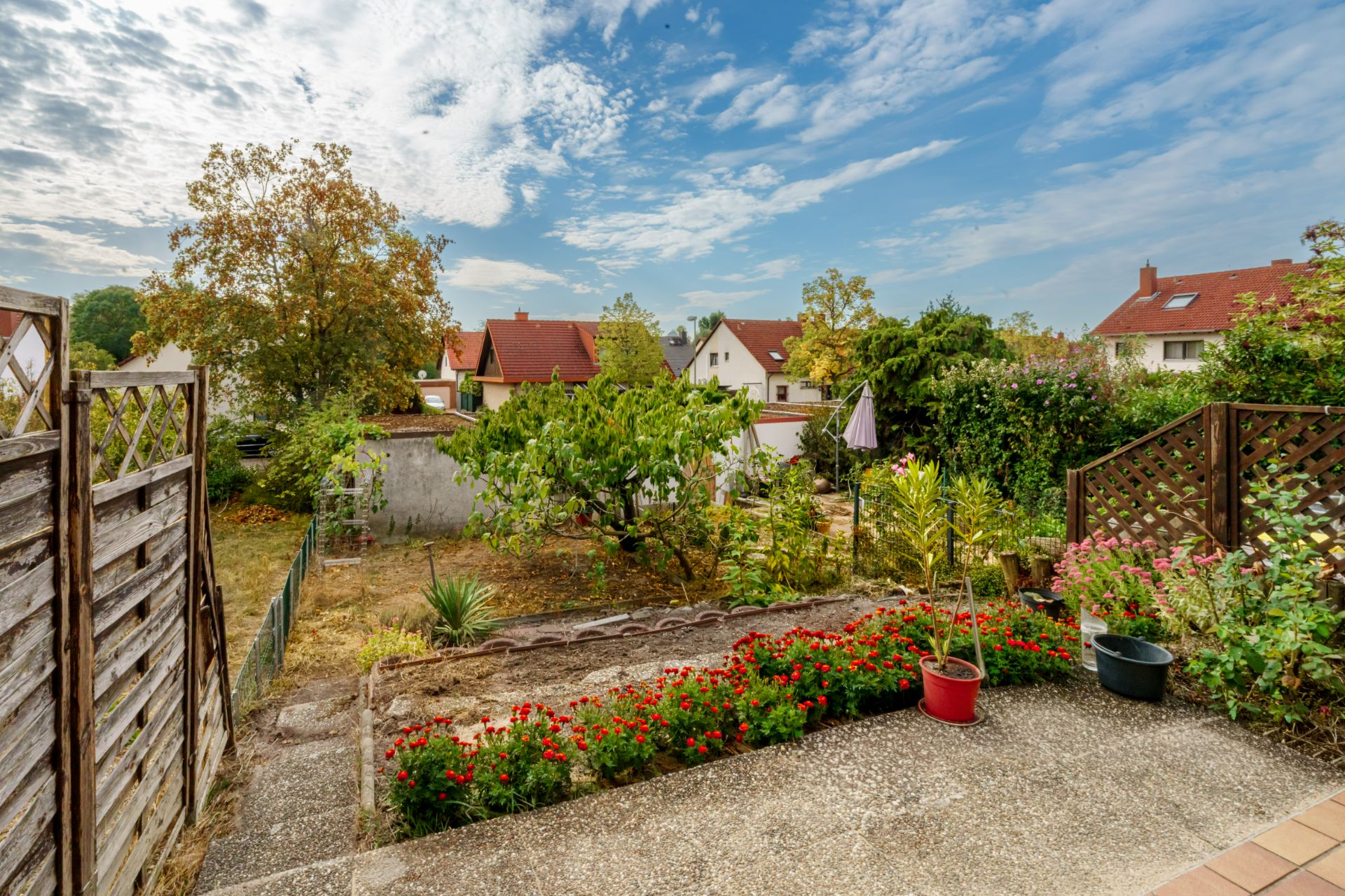 Blick von einer Terrasse auf einen Garten mit Blumen, Pflanzen und Holzzäunen in einem Wohngebiet.