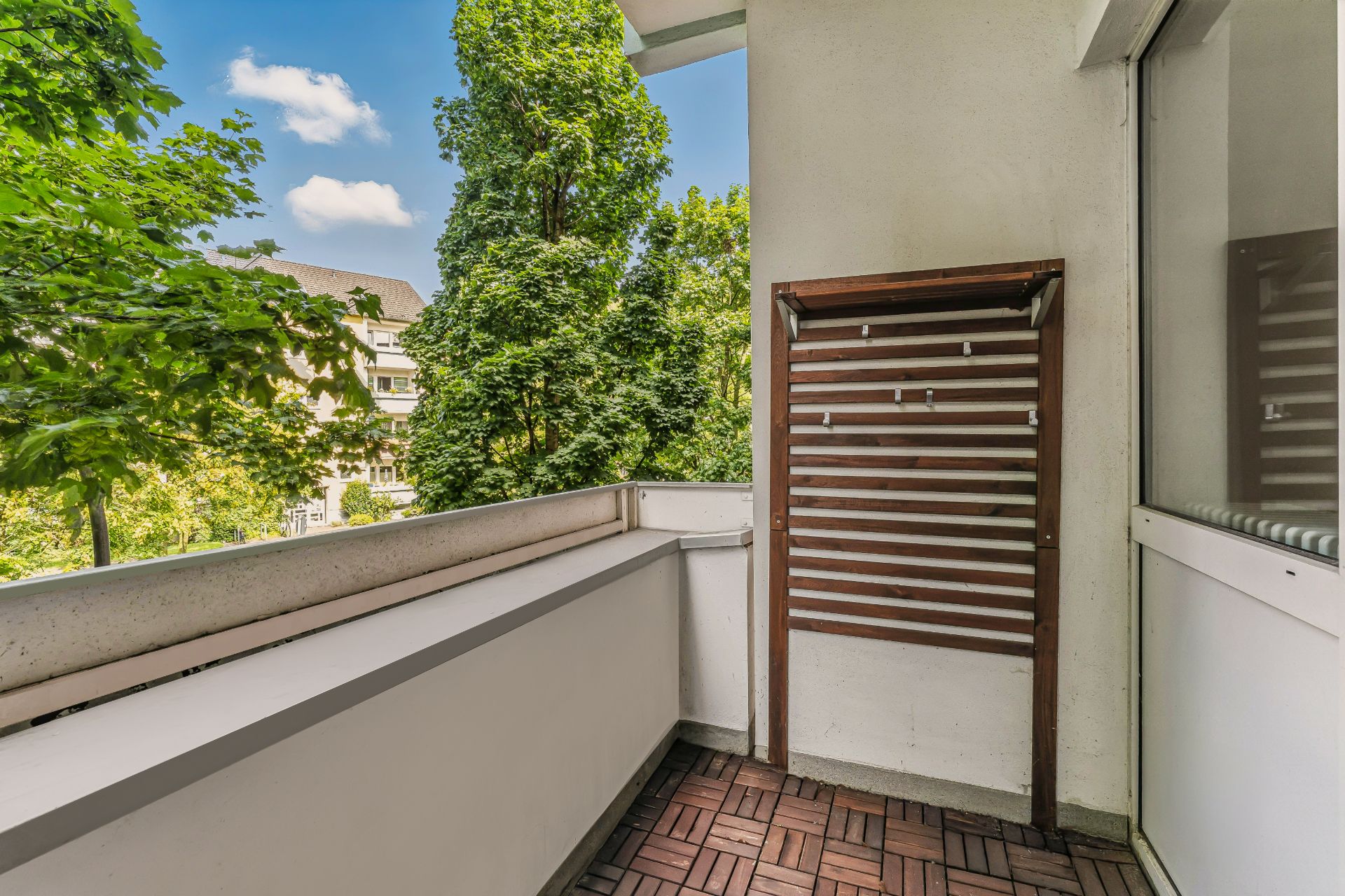 Balkon mit Holzboden und Holzgestell, umgeben von Bäumen und Blick ins Grüne.