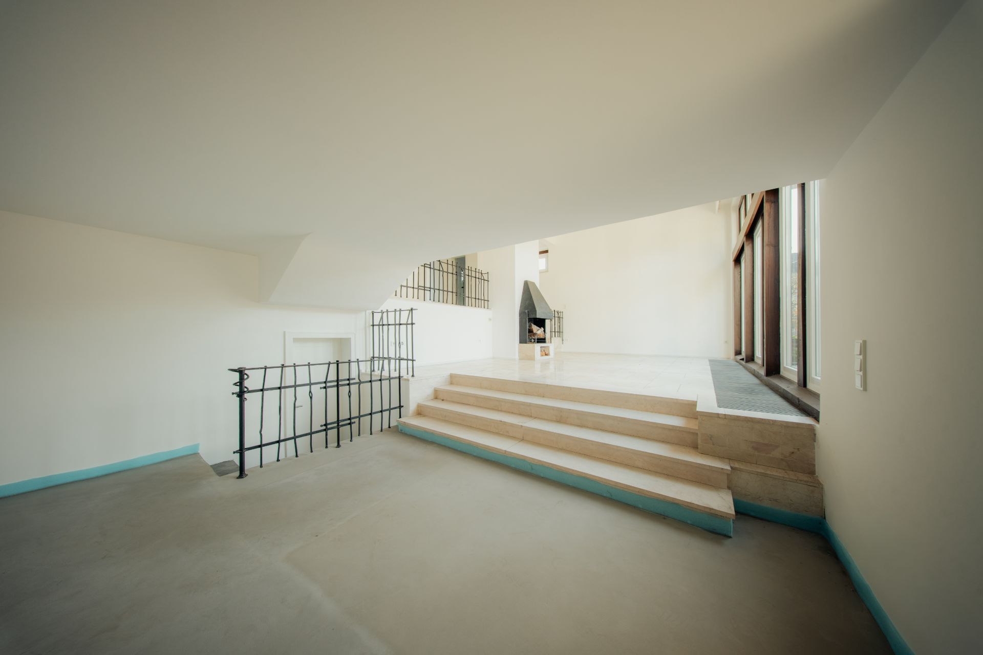 Innenraum mit Treppe, weißen Wänden, großem Fenster und Geländer aus Metall.