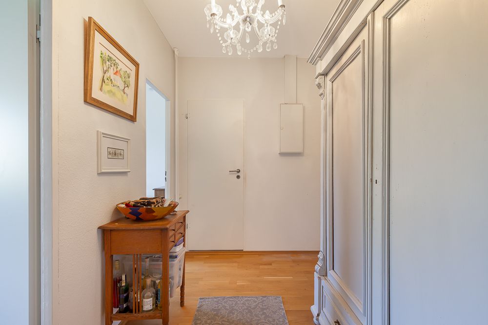 Heller Flur mit Holzboden, Kronleuchter, Kommode und großem Schrank.