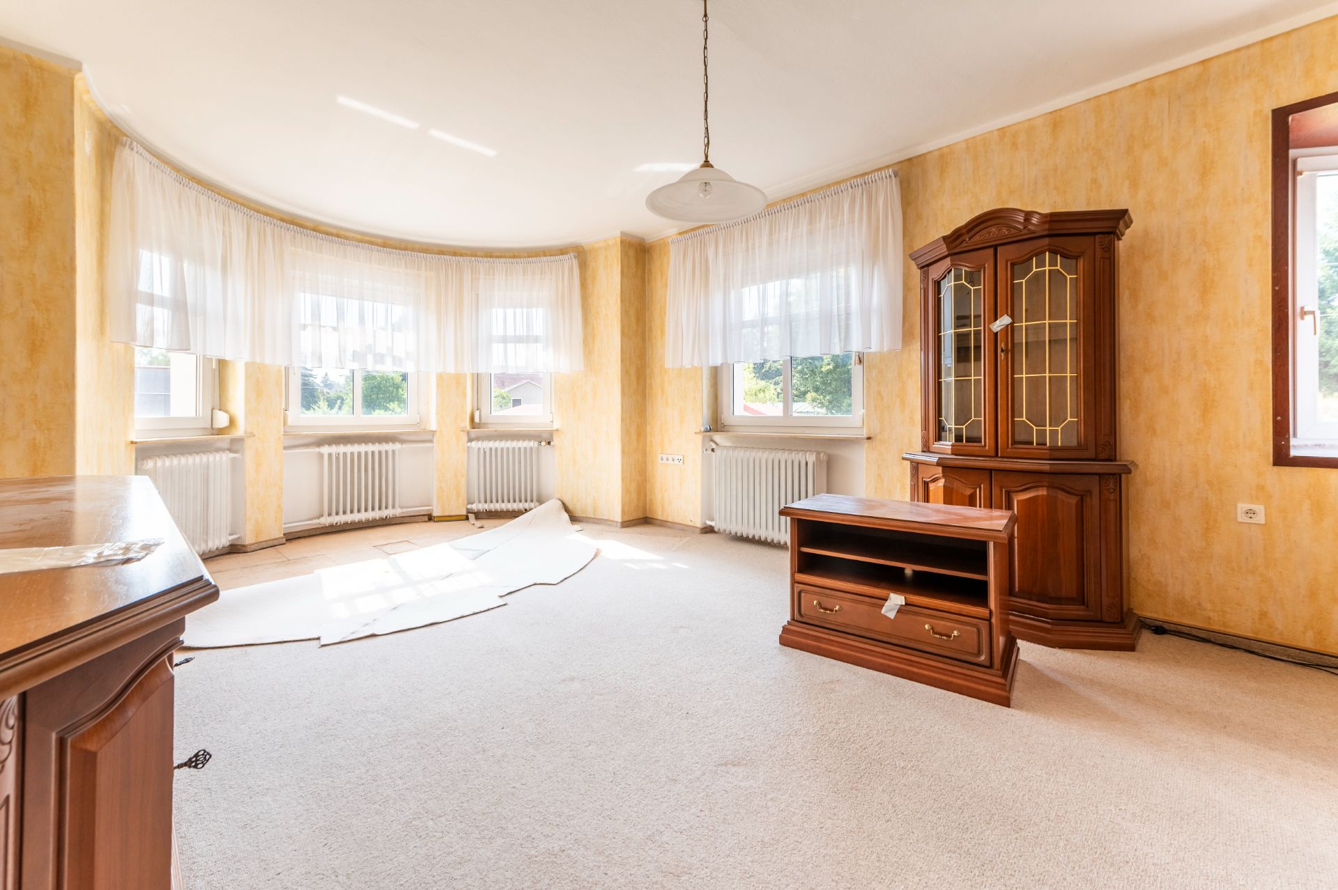 Helles Wohnzimmer mit großen Fenstern, gelben Wänden und einigen Holzmöbeln.