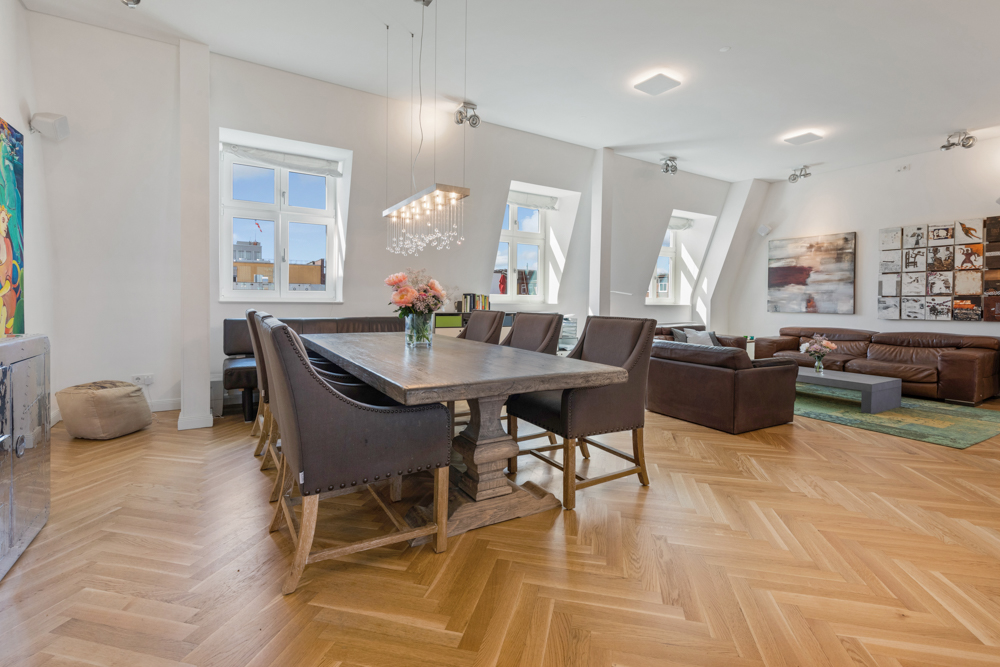 Helles Wohnzimmer mit Holzboden, Esstisch, Polsterstühlen und braunen Ledersofas.