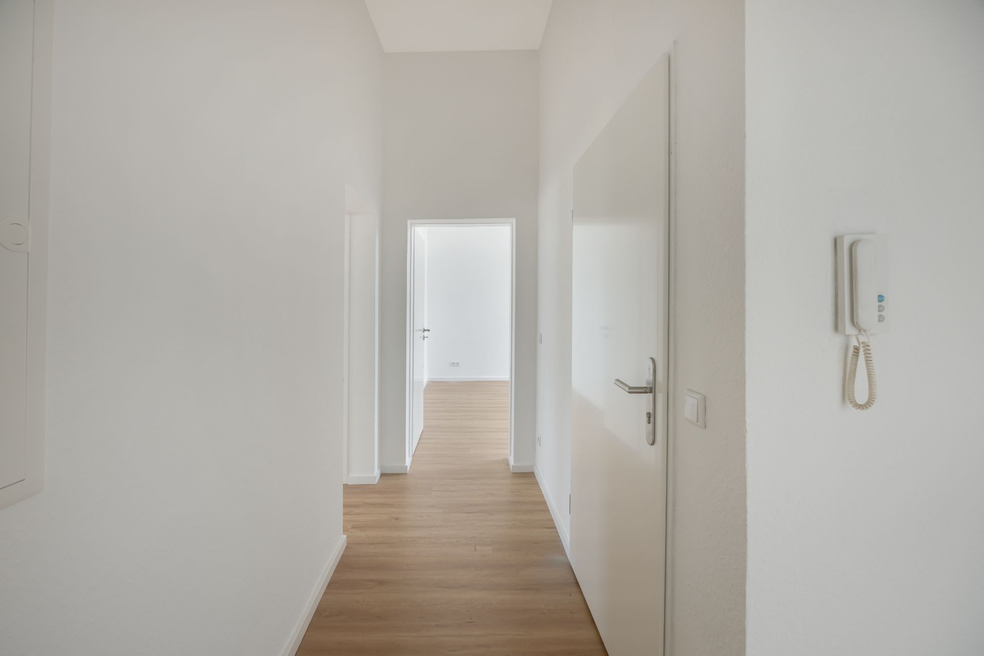 Heller Flur mit Holzboden, weißen Wänden und einer offenen Tür im Hintergrund.