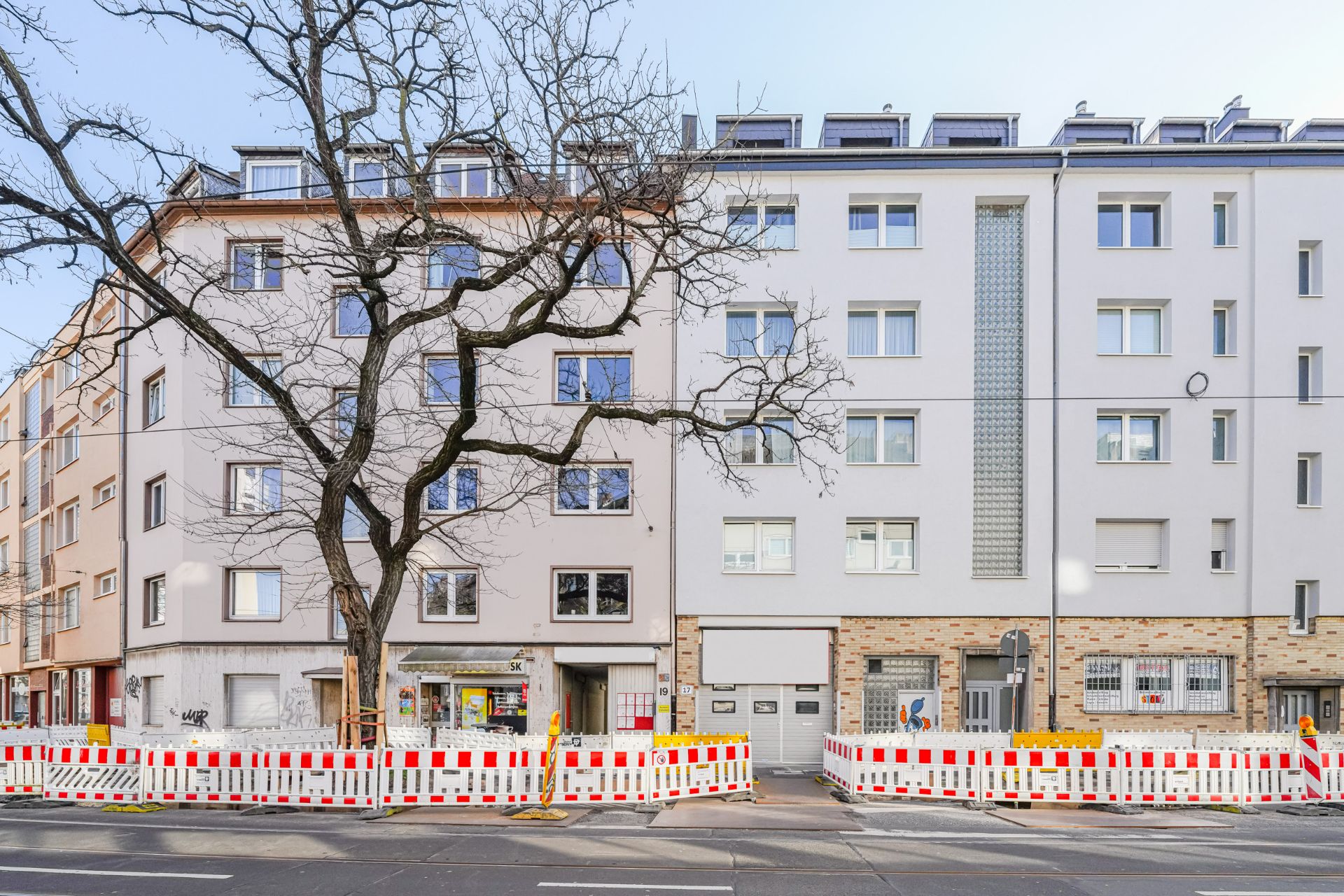 Mehrstöckige Wohnhäuser mit Bauzäunen und einem kahlen Baum davor.