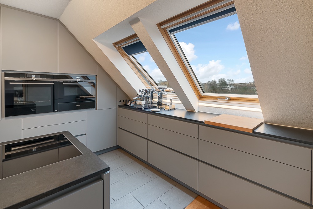 Moderne Küche mit Einbaugeräten, großer Arbeitsfläche und zwei Dachfenstern mit Ausblick.