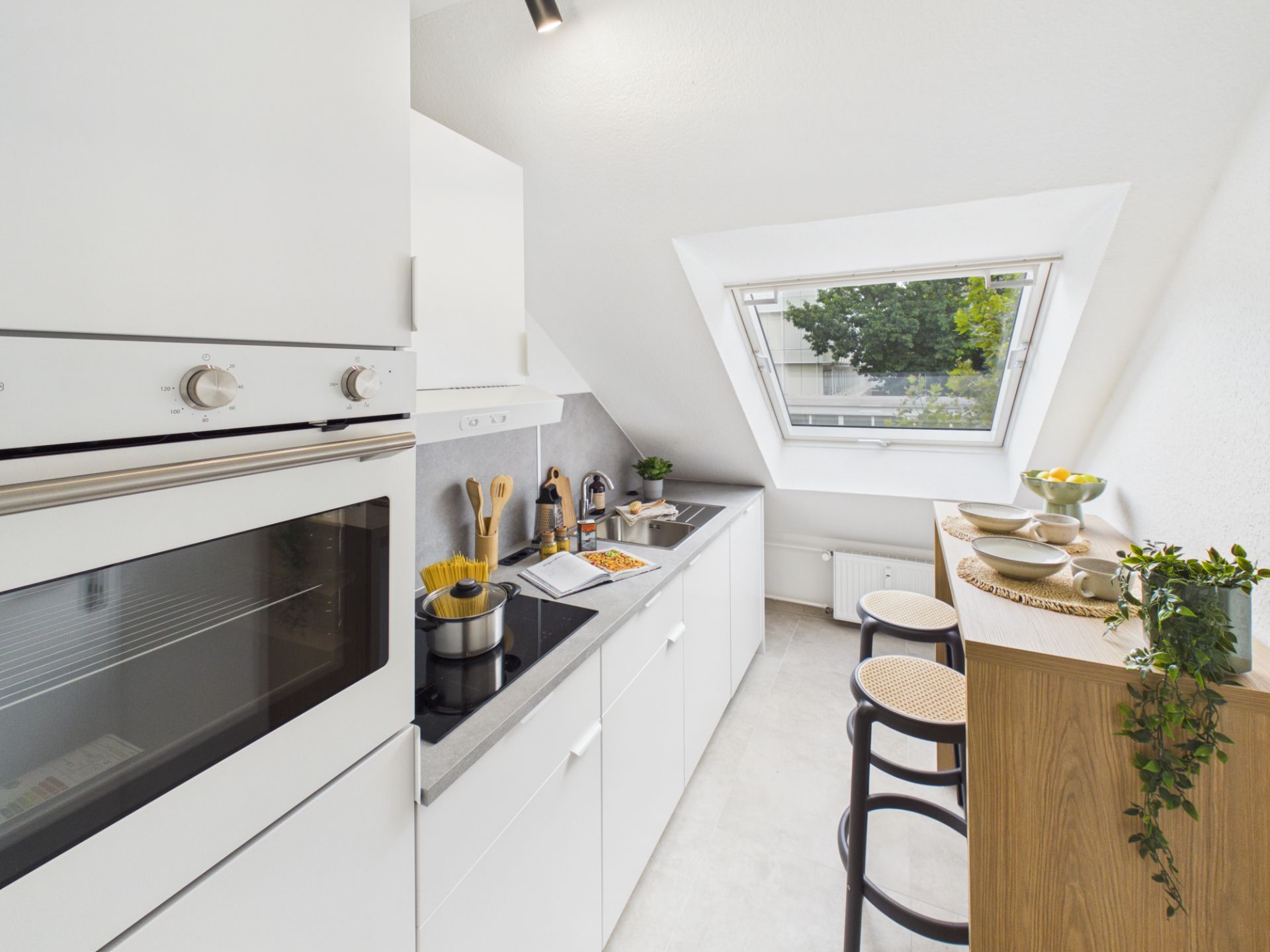 Moderne, schmale Küche mit weißen Schränken, Herd, Backofen und großem Fenster im Dachgeschoss.